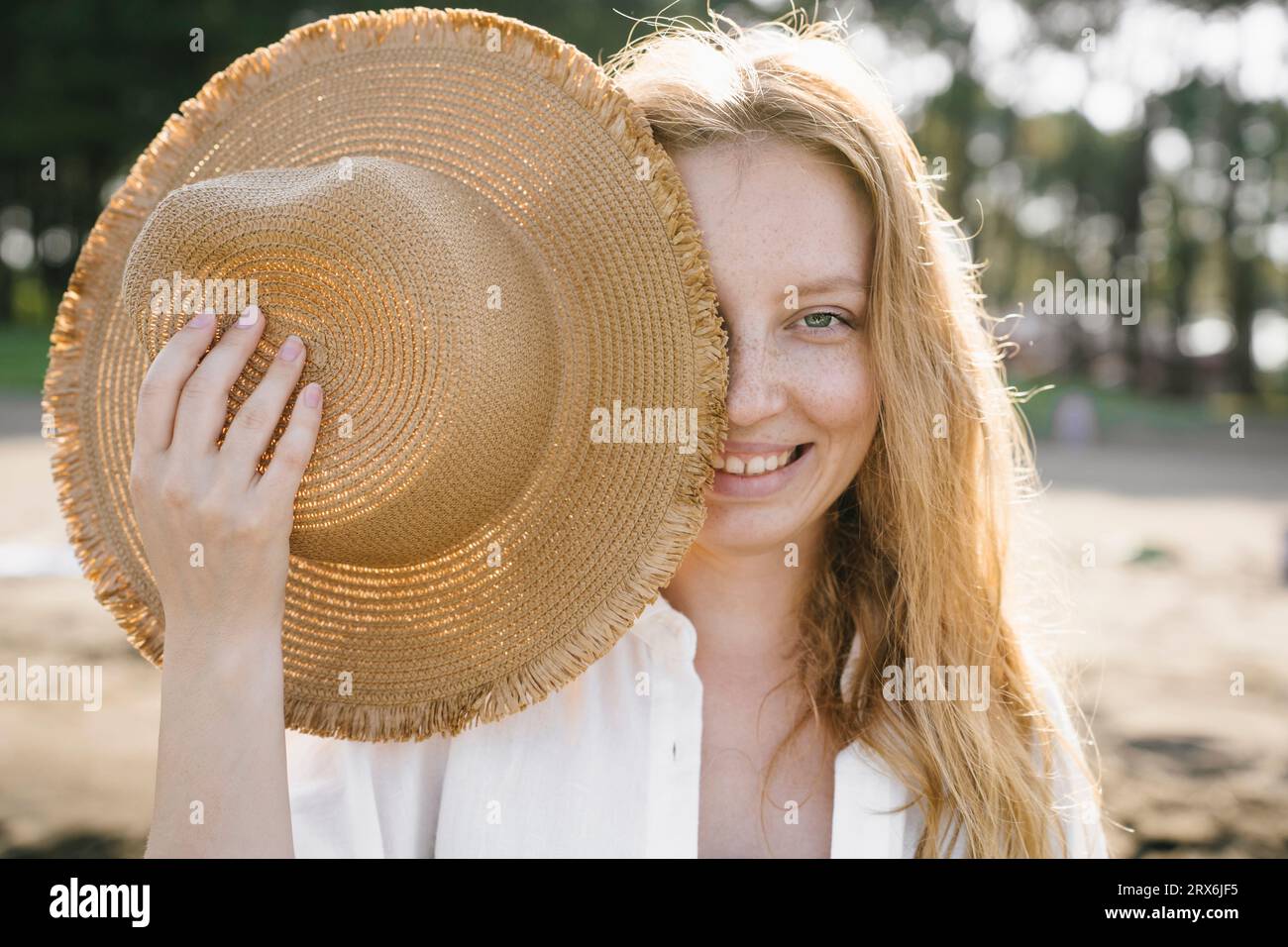 Femme blonde cachant le visage avec le chapeau de soleil à la plage Banque D'Images