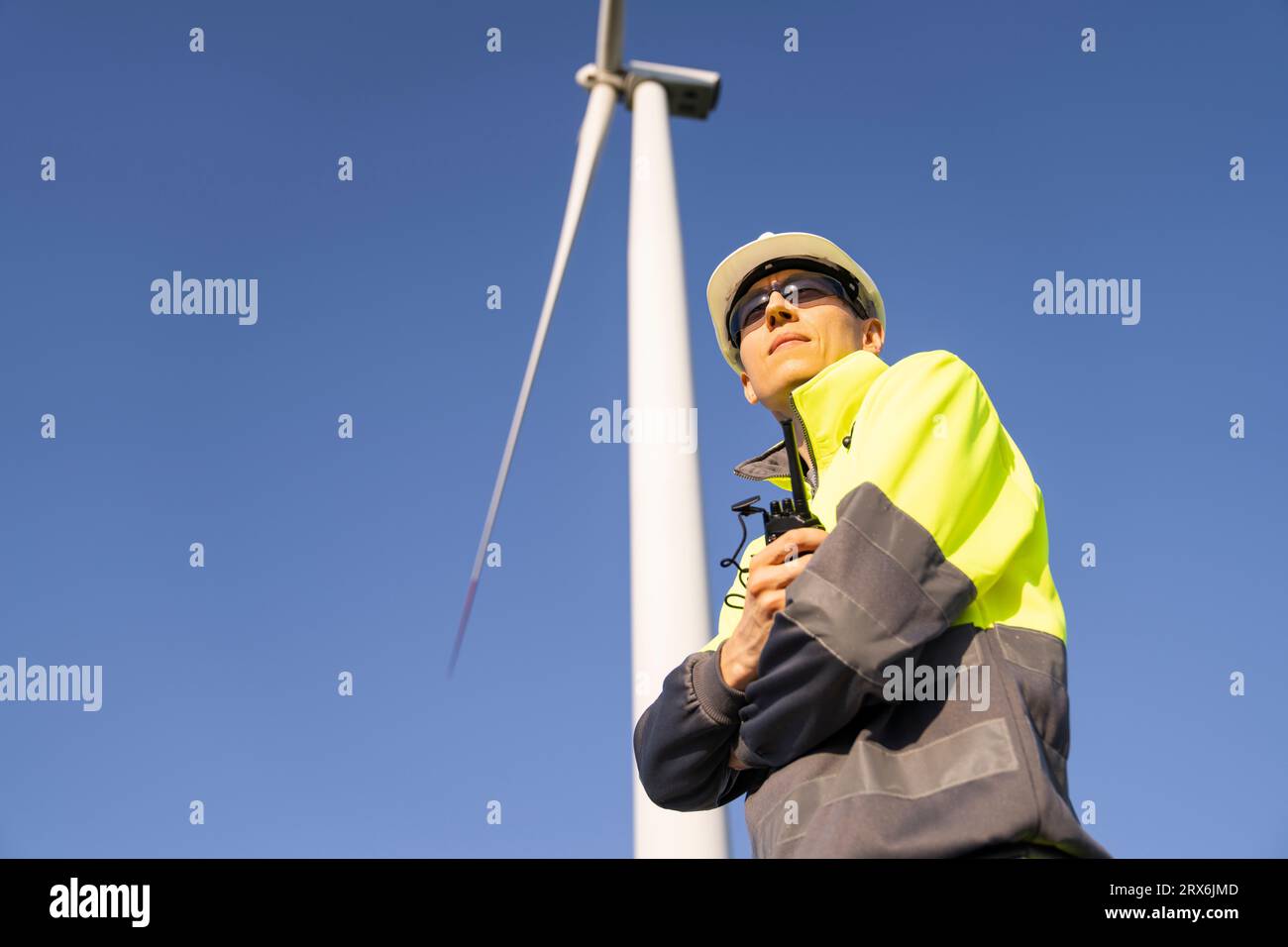 Ingénieur réfléchi debout avec les bras croisés sous l'éolienne Banque D'Images