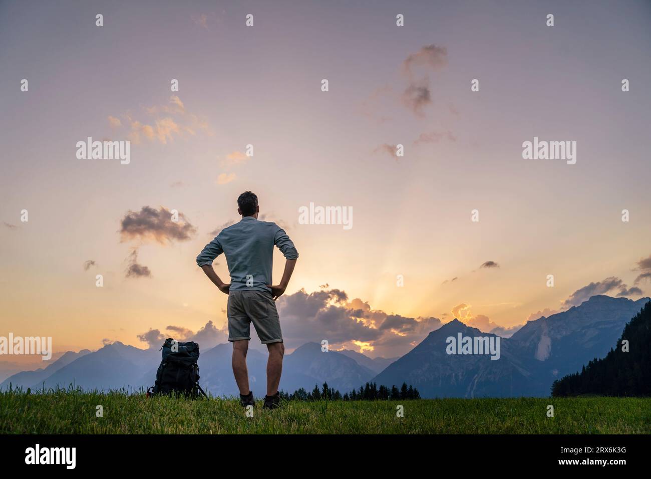 Randonneur avec les mains sur les hanches regardant les montagnes dans la prairie Banque D'Images