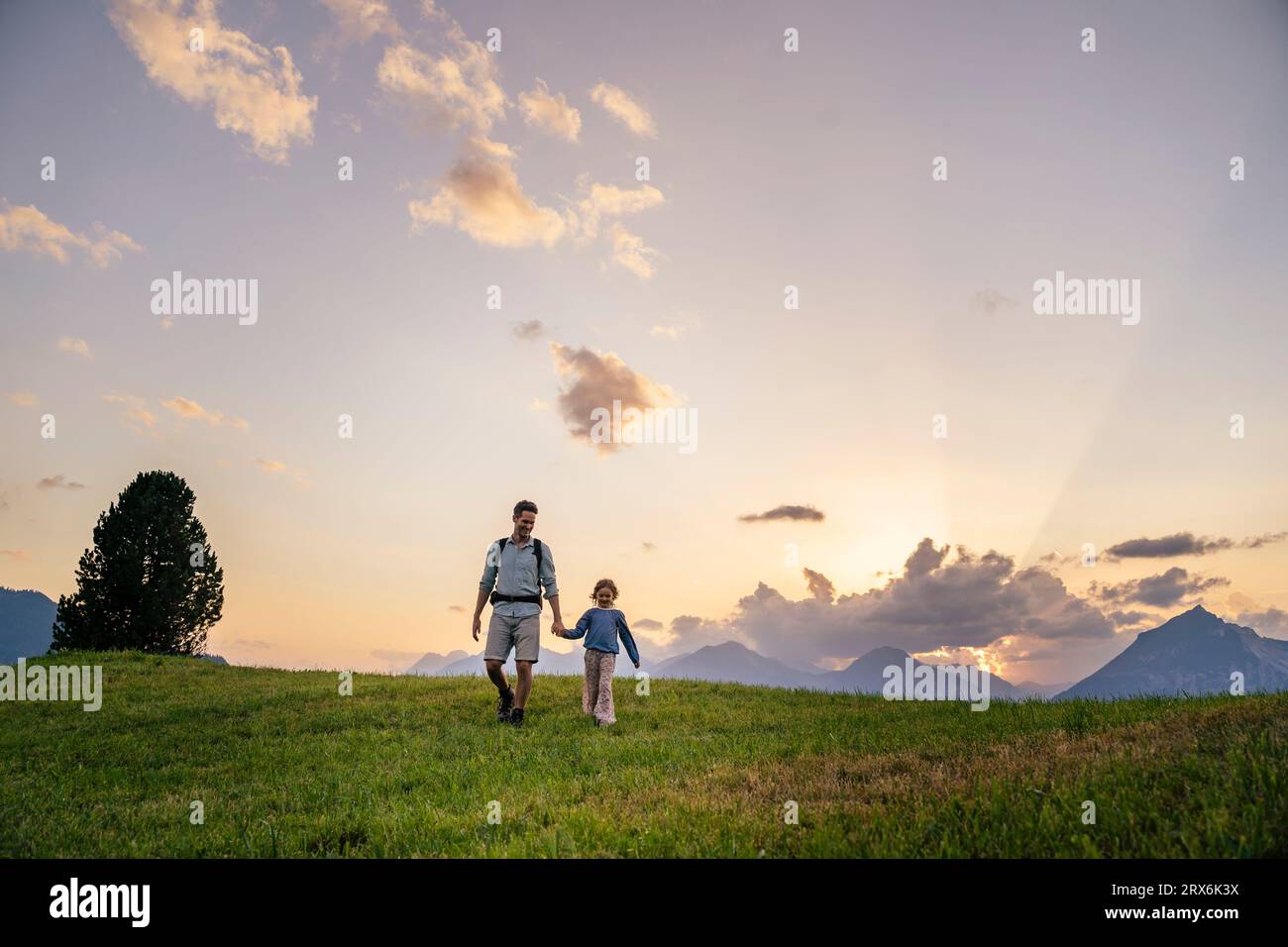 Père et fille marchant sur l'herbe devant les montagnes Banque D'Images