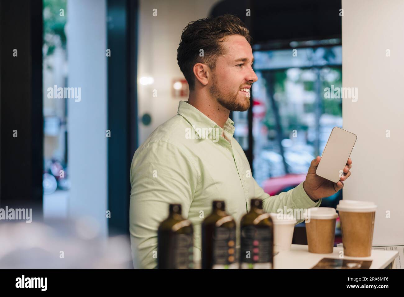 Jeune homme d'affaires souriant avec téléphone intelligent dans le café Banque D'Images