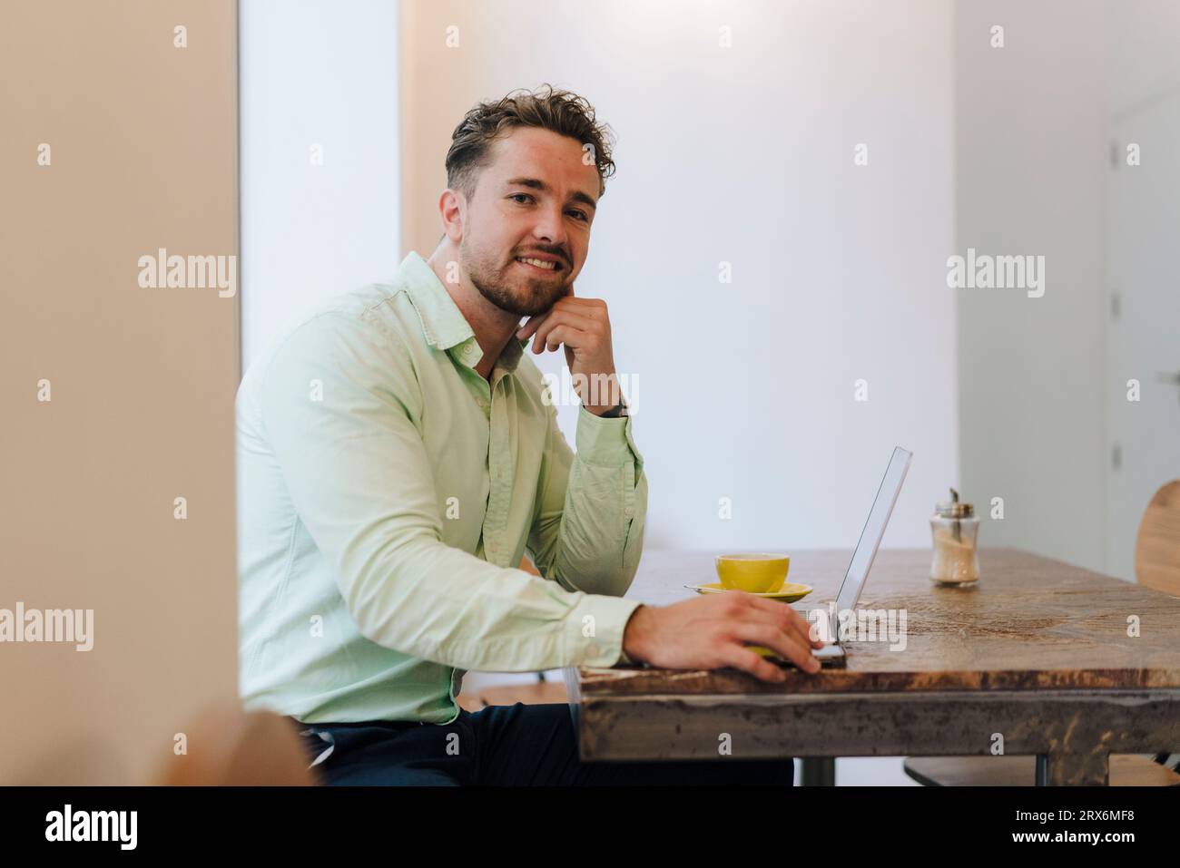 Jeune homme d'affaires souriant assis avec ordinateur portable dans le café Banque D'Images