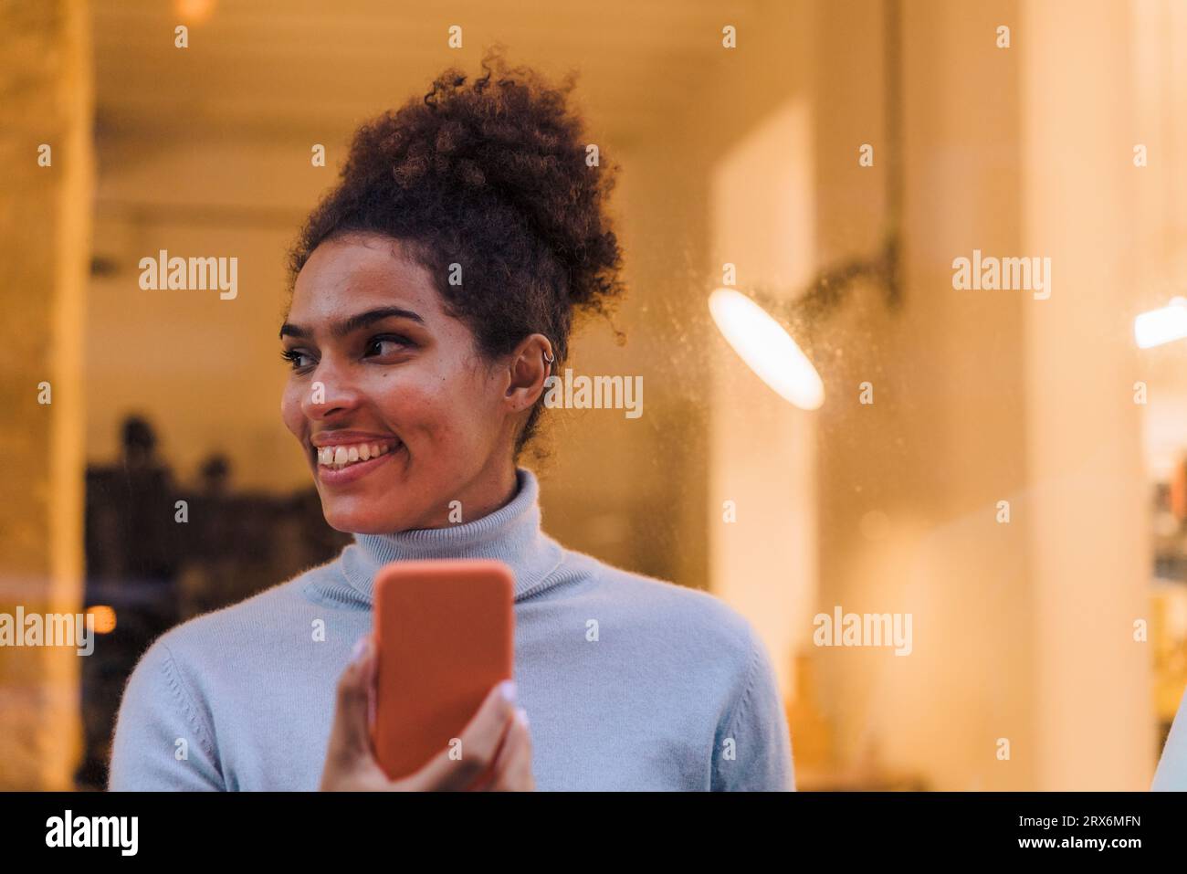 Jeune femme souriante avec téléphone intelligent devant le verre Banque D'Images