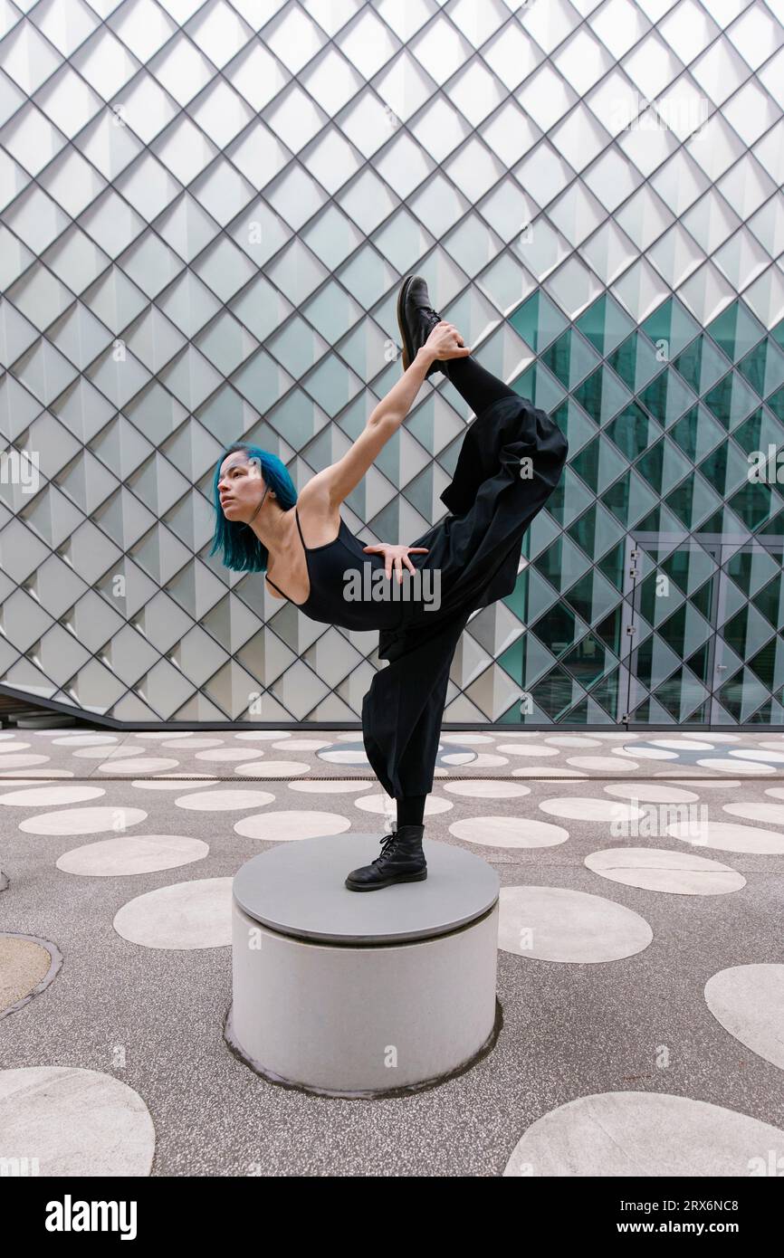 Jeune danseur flexible dansant sur un siège en béton circulaire devant un bâtiment moderne Banque D'Images