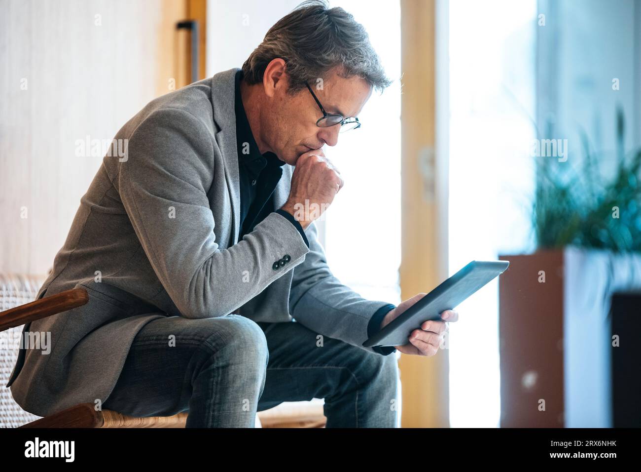 Homme d'affaires avec la main sur le menton à l'aide d'une tablette PC dans le bureau Banque D'Images
