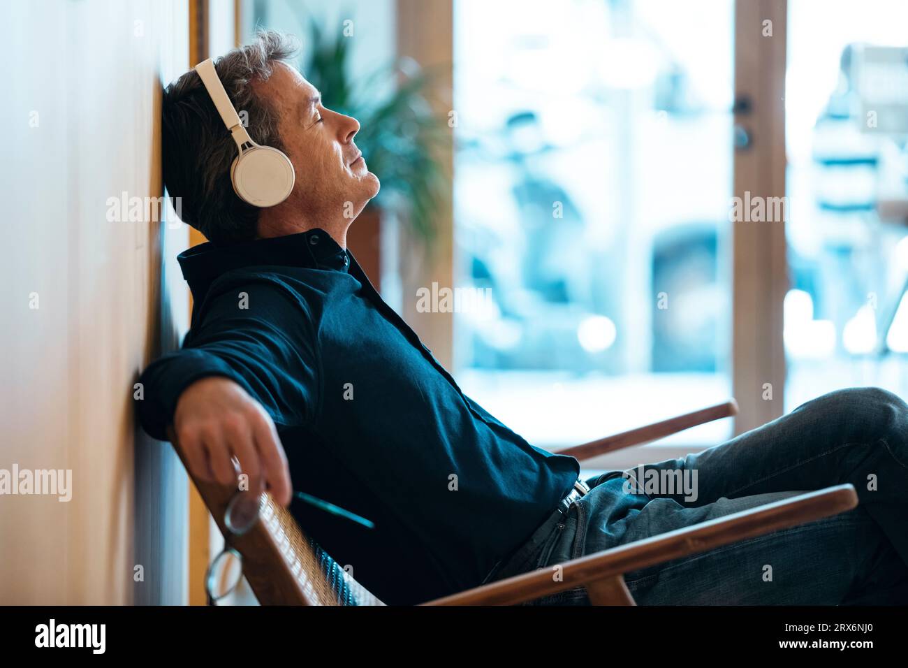 Homme mature portant des écouteurs sans fil assis dans un fauteuil Banque D'Images