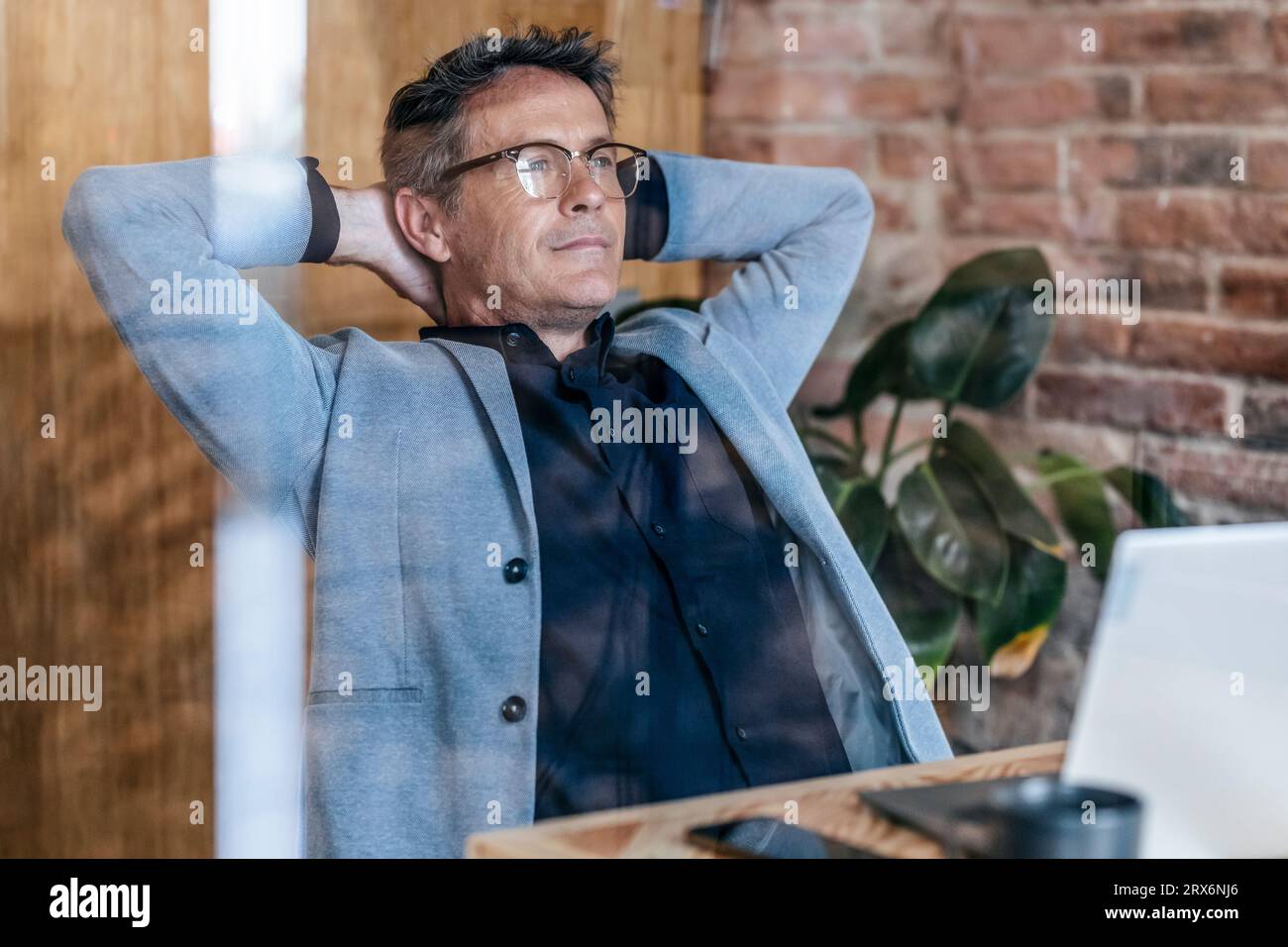 Homme d'affaires réfléchi assis avec les mains derrière la tête dans le bureau Banque D'Images