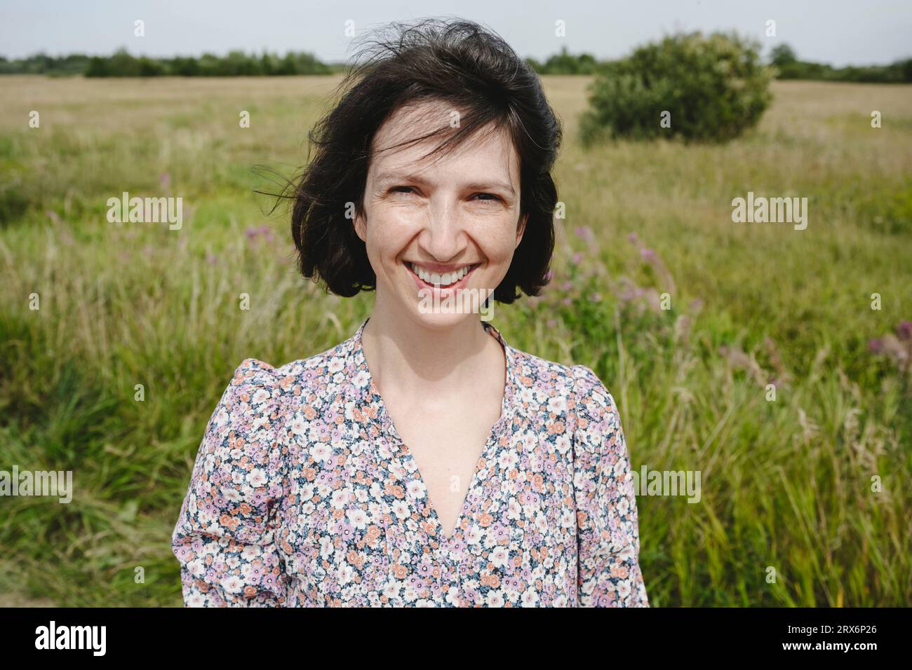 Femme souriante debout devant l'herbe le jour ensoleillé au champ Banque D'Images