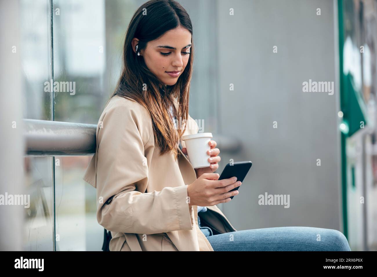 Jeune femme avec tasse à café à l'aide d'un téléphone intelligent Banque D'Images