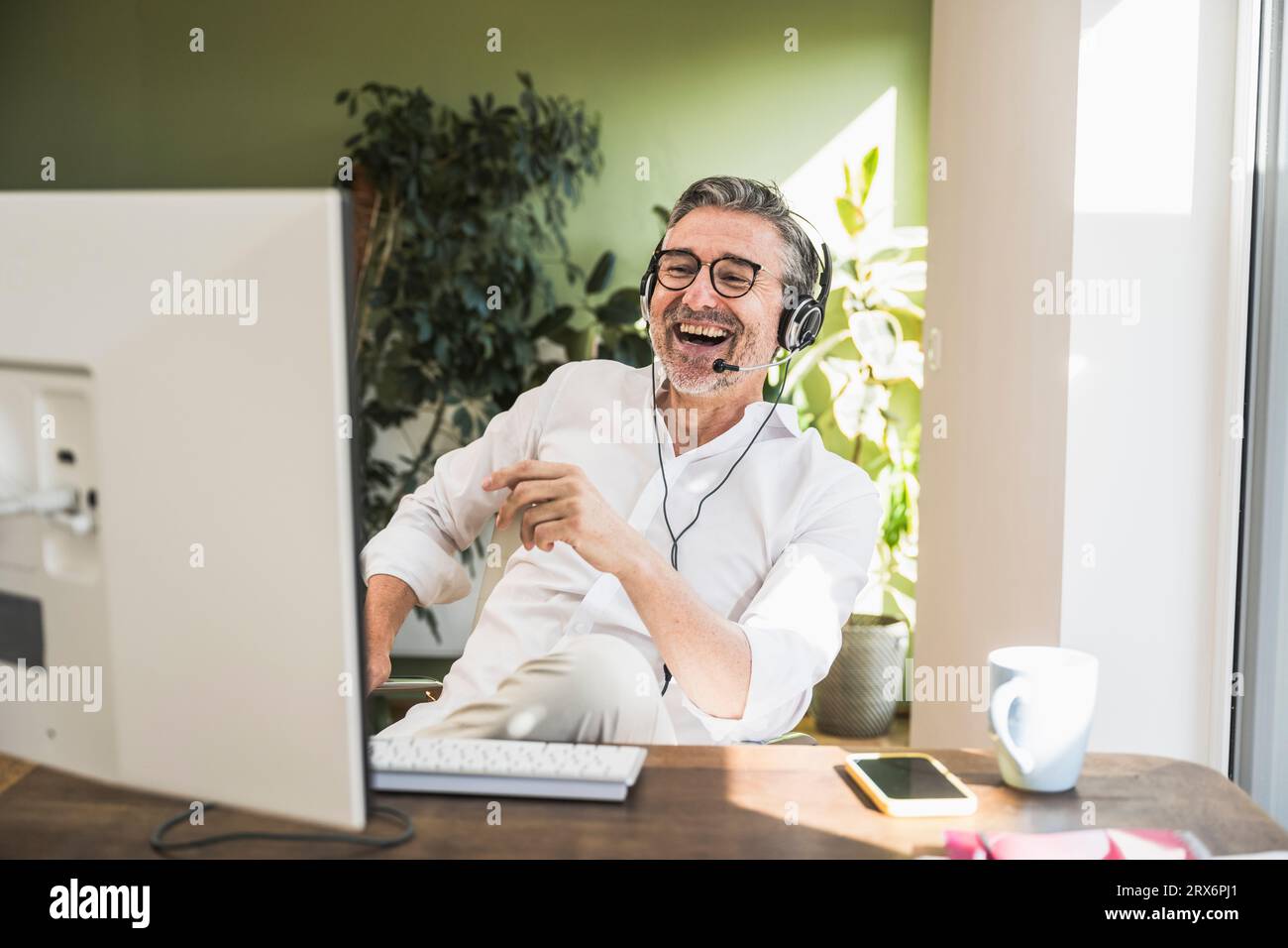 Représentant du service clientèle riant et parlant au-dessus de son micro-casque au bureau à domicile Banque D'Images