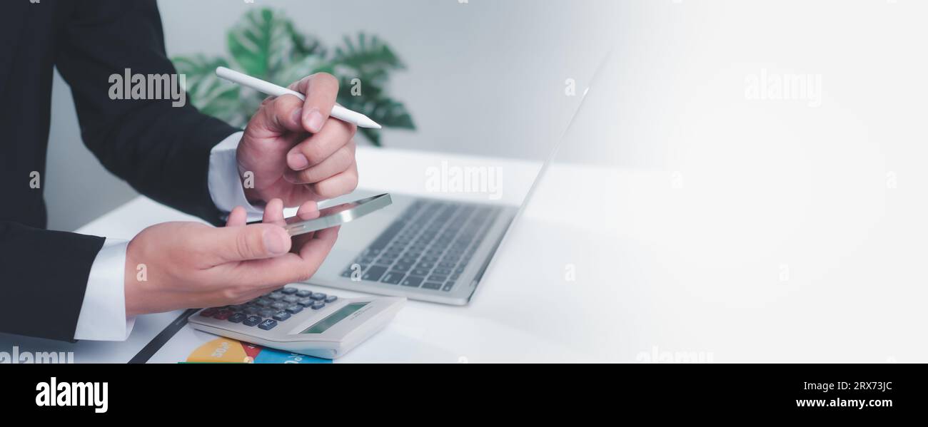 Homme d'affaires tenant un stylo et smartphone travaille sur une table blanche avec un ordinateur dessus. Sur fond blanc avec espace de copie. Banque D'Images