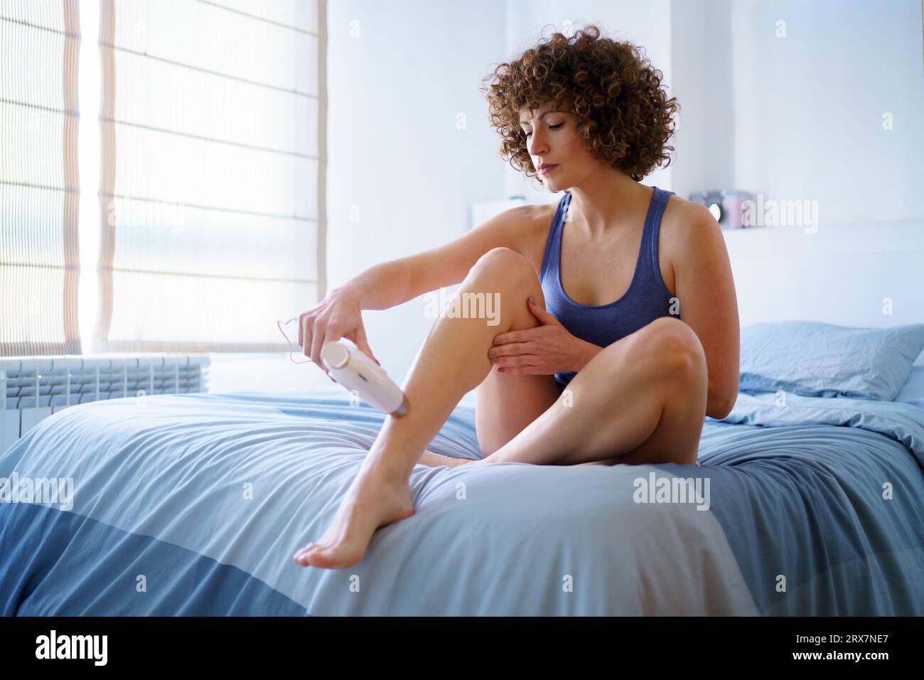 Femme adulte faisant l'épilation au laser à la jambe sur le lit Banque D'Images