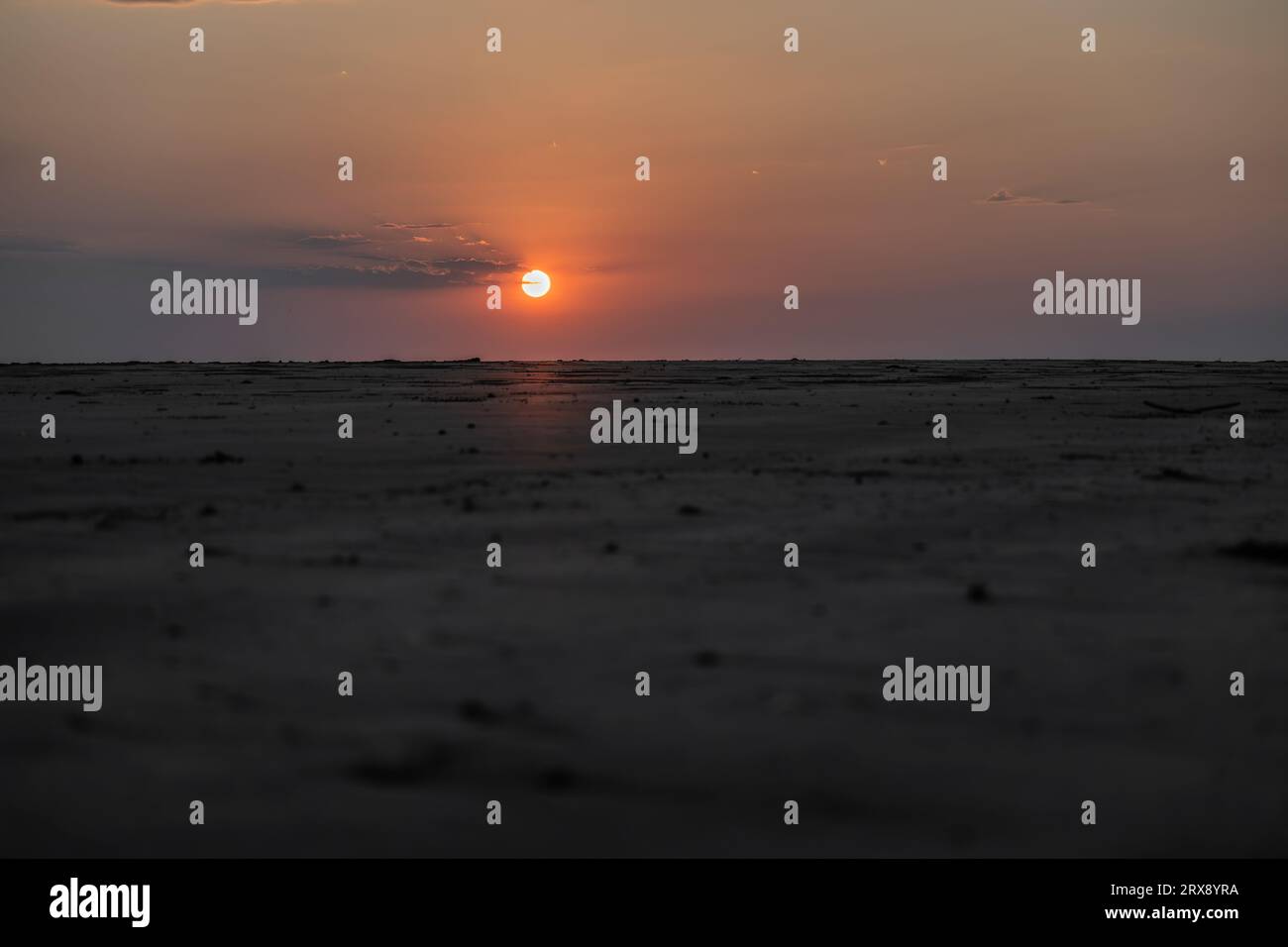 Le soleil se couche à l'horizon derrière une colline de plage sablonneuse en Australie, créant une atmosphère autre-monde. Banque D'Images