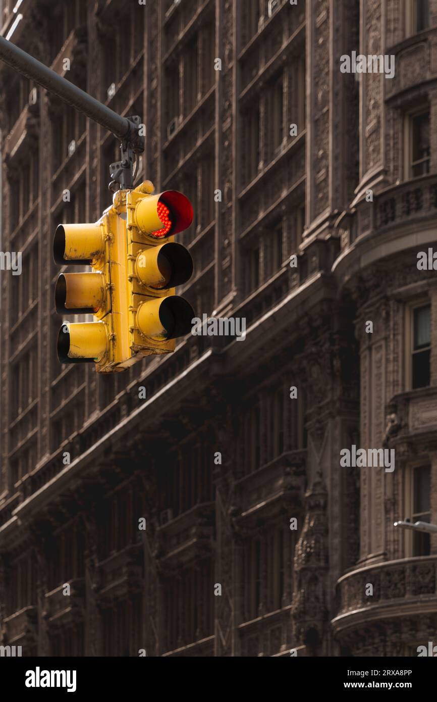 Un feu stop rouge affiché sur un feu de circulation jaune à l'intersection d'une rue et d'une avenue à New York City avec un vieux fond de bâtiment avec Banque D'Images