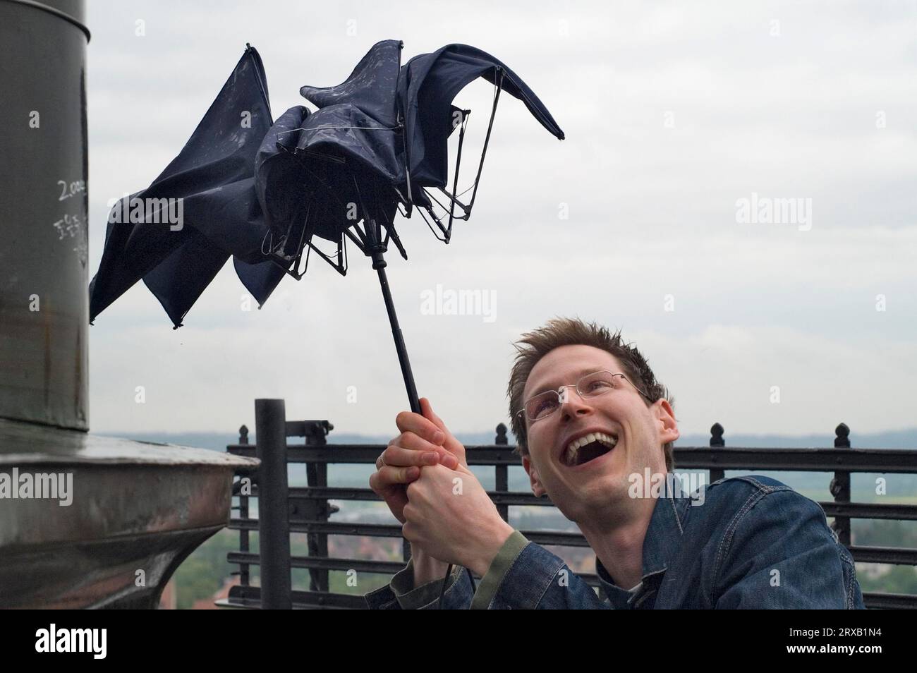 Manipulation ludique d'un jeune homme lors de l'effondrement d'un parapluie bon marché par un squall sur une tour Banque D'Images
