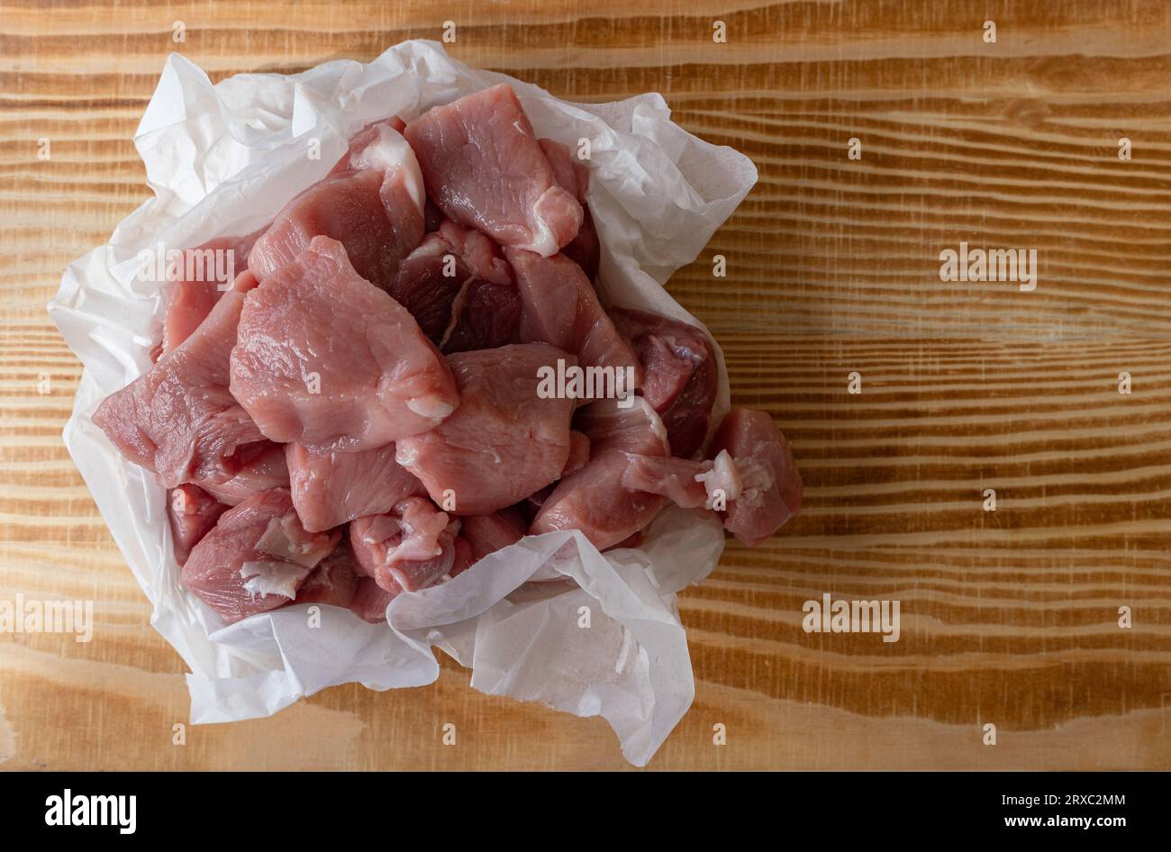 Cuisse de porc coupée en dés emballée dans du papier blanc sur une table en bois. Banque D'Images