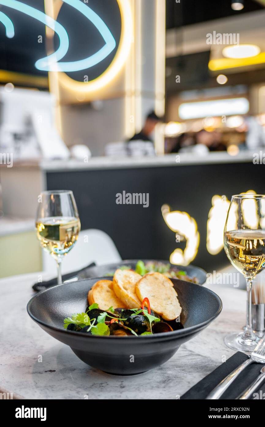 Moules en sauce crème avec croûtons dans une assiette noire sur une table dans un restaurant avec un verre de vin blanc Banque D'Images