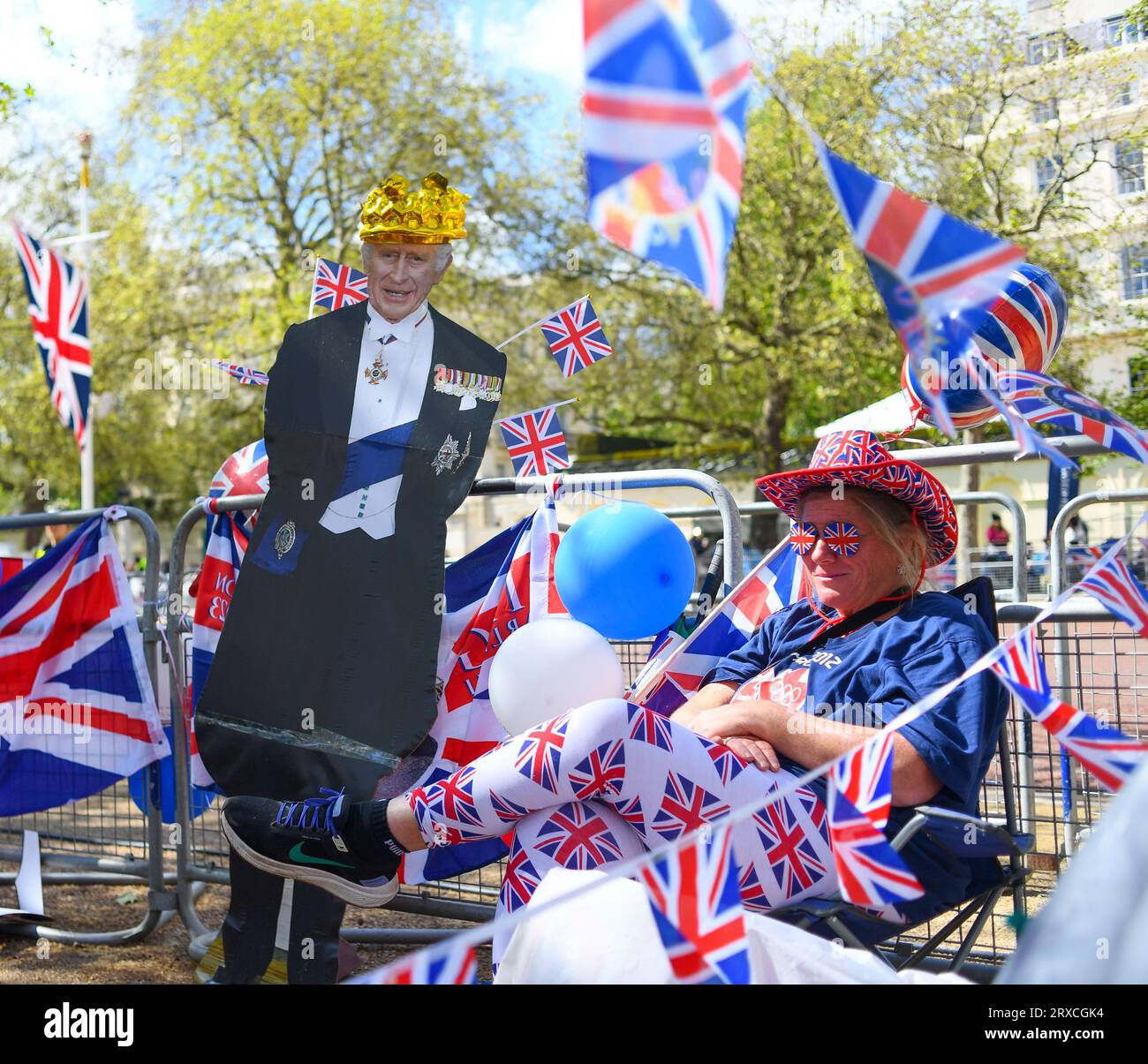 Une dame est assise à côté d'un carton découpé dans le roi Charles entouré de drapeaux de l'Union Jack ayant sécurisé sa place sur le Mall à Londres avant l'événement Banque D'Images