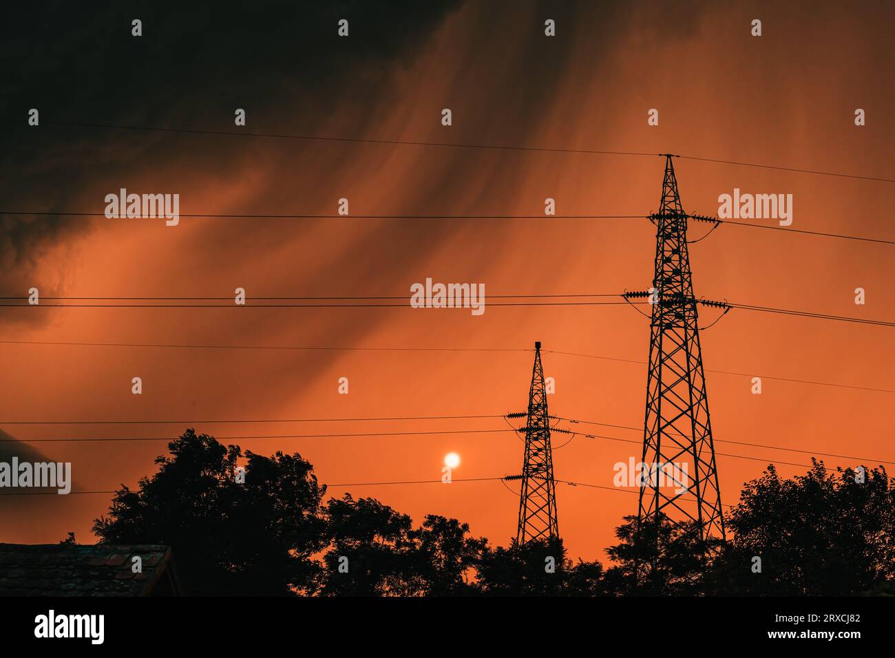 Nuages orageux sombres au ciel orange d'été, silhouettes de cimes d'arbres et pylône électrique juste avant la pluie, mise au point sélective Banque D'Images