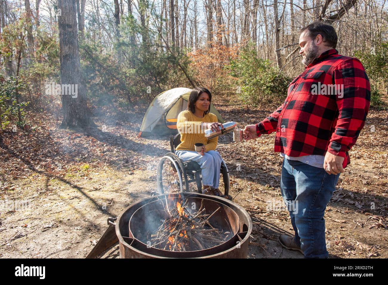 Un couple outdoorsy partage une boisson chaude pour rester au chaud dans leur camping. Les deux sont handicapés mais adorent le plein air. Banque D'Images