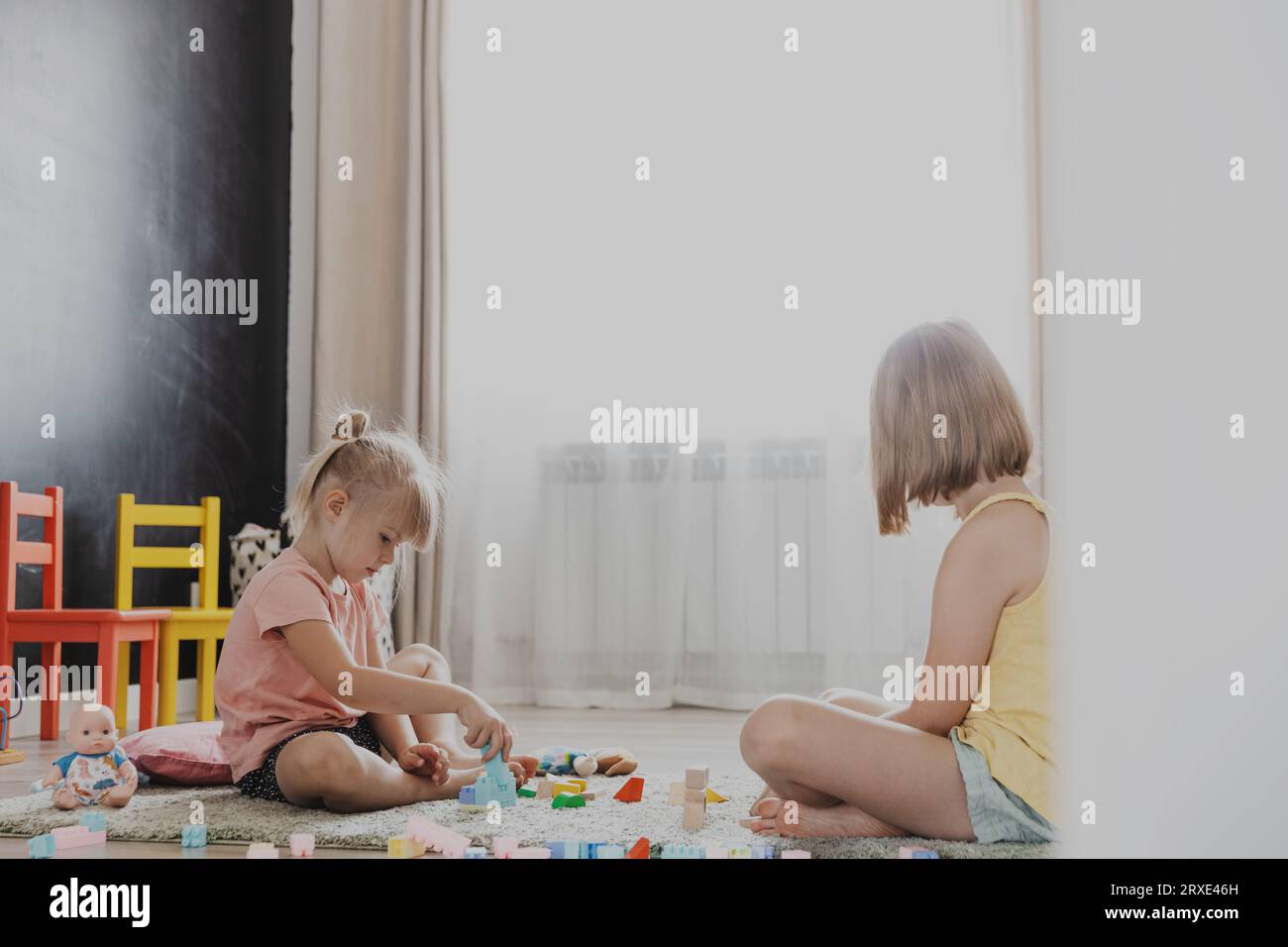 Enfants jouant avec des blocs de construction de jouets en bois colorés, briques. Enfants assis sur le sol à la chambre à coucher blanche ensoleillée ou à la maternelle, salle de jeux de garderie Banque D'Images