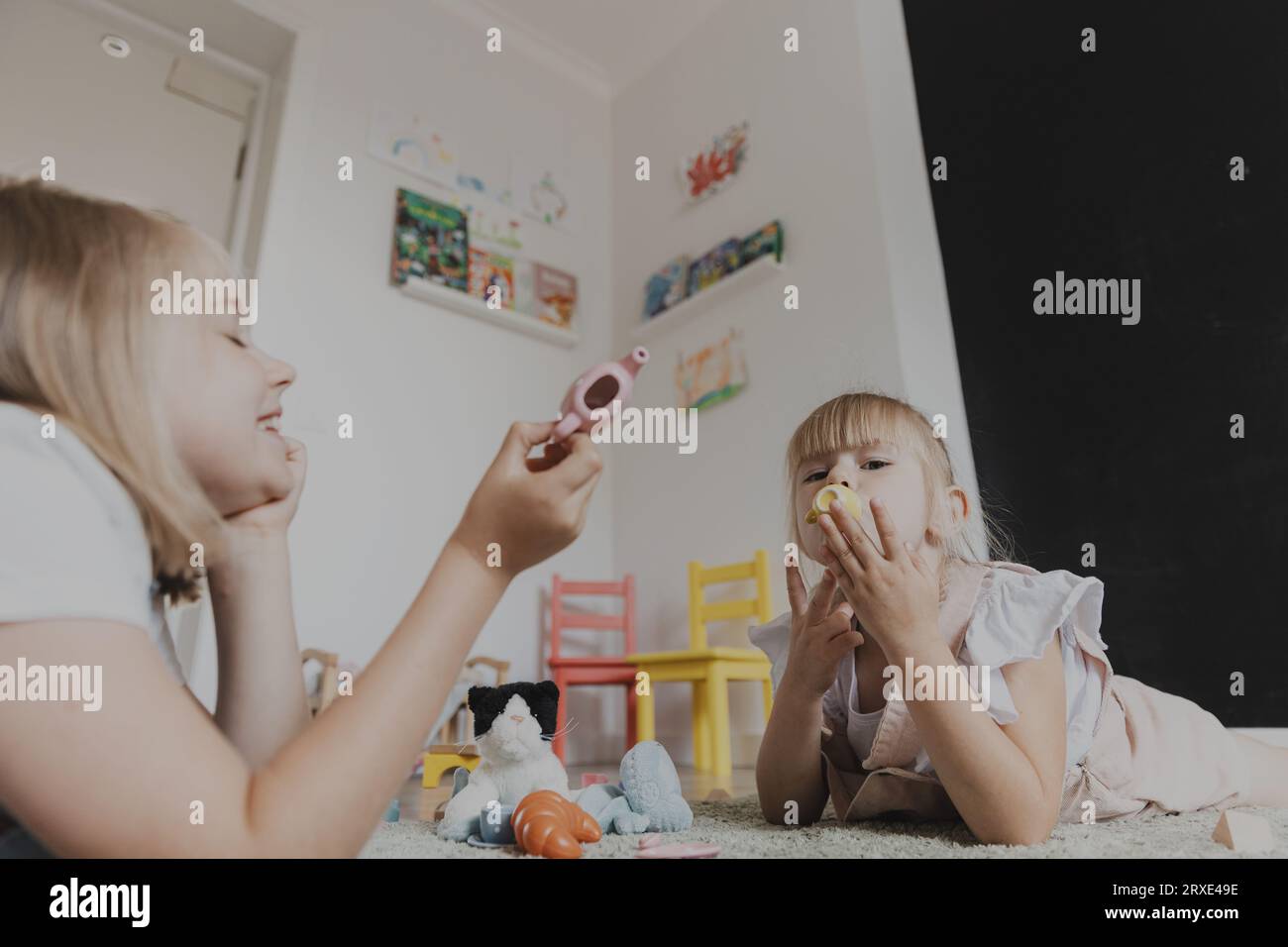 Gros plan d'enfants de sexe féminin jouant avec un ensemble de thé de jeu de jouet coloré. Enfants couchés sur la moquette à la chambre à coucher ou à la maternelle. gam écologique éducatif Banque D'Images