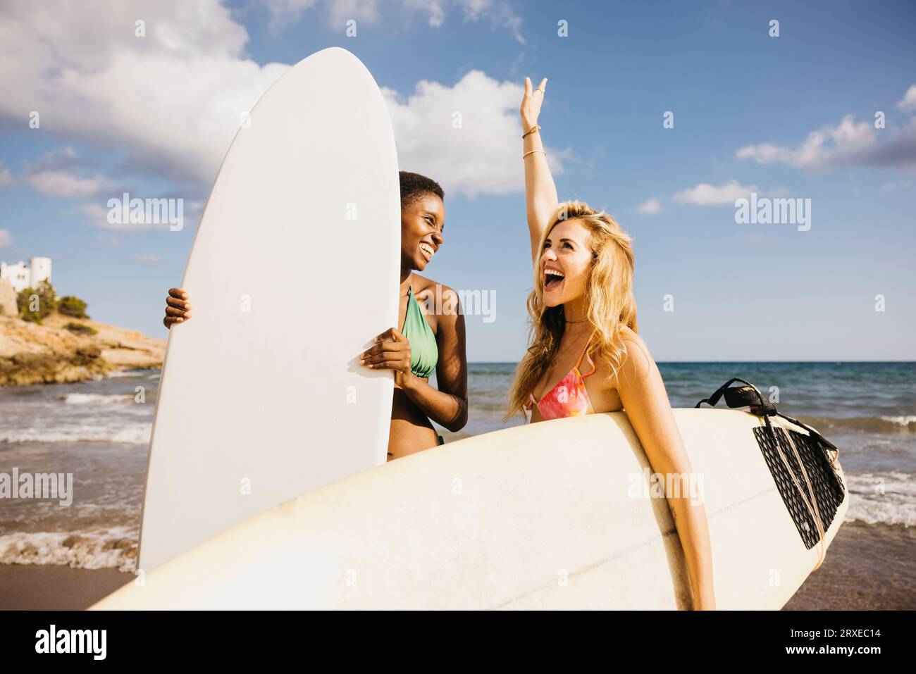 Deux amies joyeuses célébrant pendant une journée de repos à la plage faisant du surf. Femmes heureuses en maillot de bain tenant leurs planches de surf sur le rivage, teami Banque D'Images
