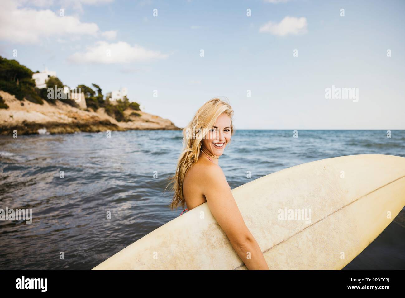 Belles femmes blondes souriantes en maillot de bain portant une planche de surf à la plage pendant des vacances amusantes au bord de la mer. Banque D'Images