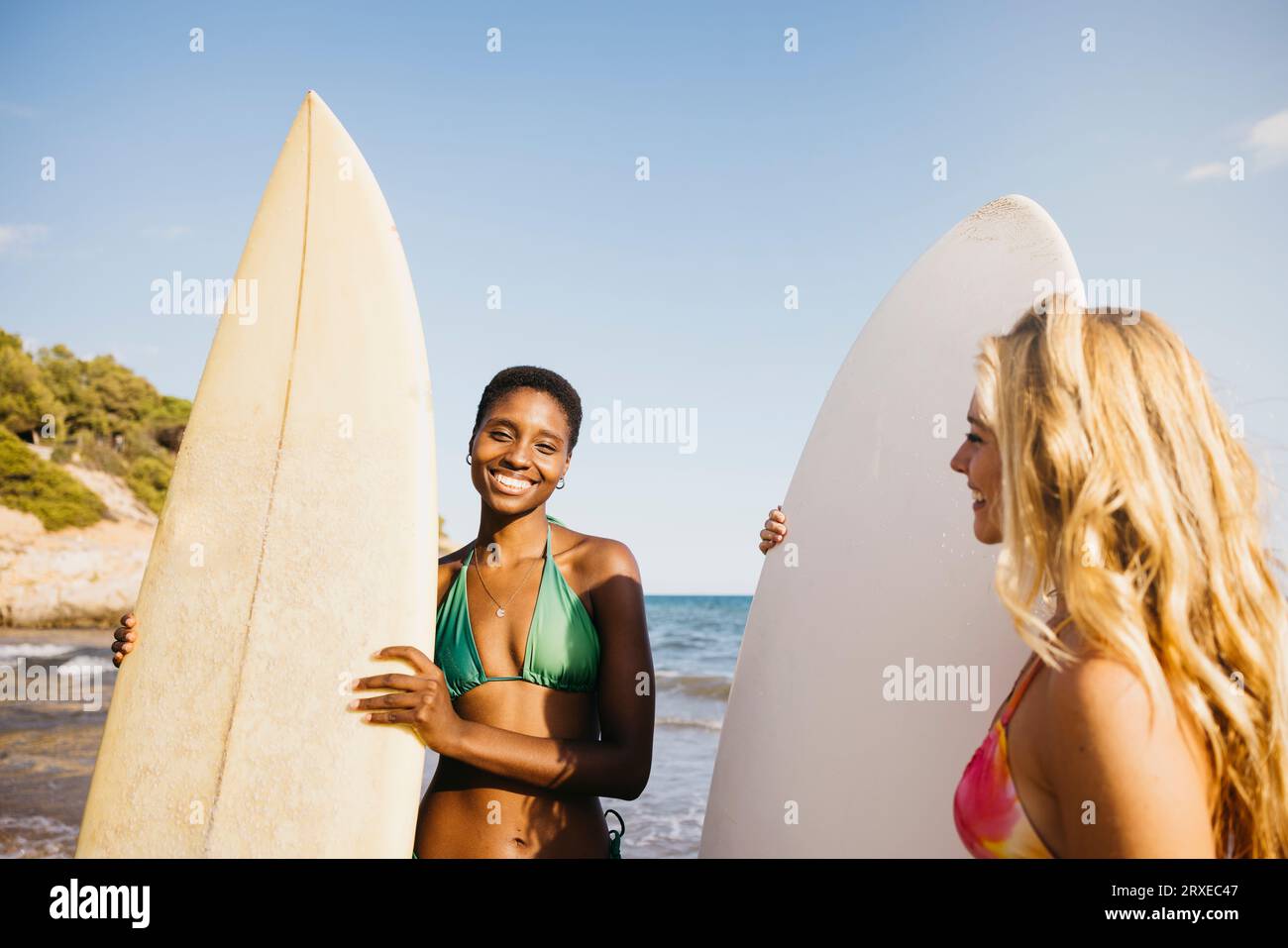 Portrait de deux amies surfeuses sur la plage en bikini, avec sa planche de surf à ses côtés. Femmes faisant des activités de plage pendant les vacances d'été. Banque D'Images