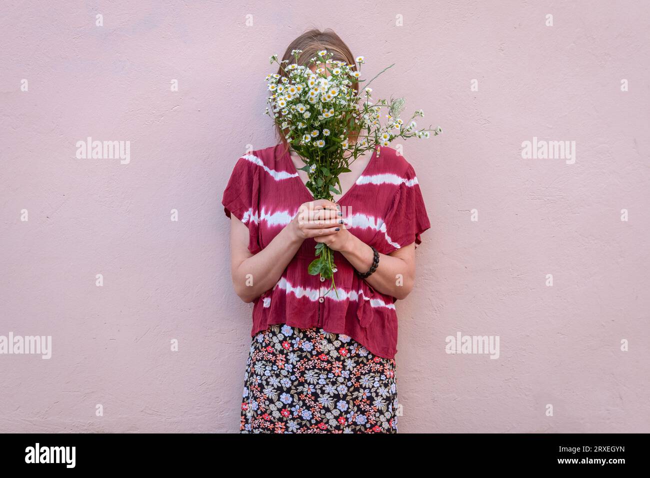 Jeune femme couvrant son visage avec bouquet de fleurs sauvages. Bouquet de fleurs blanches couvrant le visage de la femme portant une jupe fleurie. Banque D'Images
