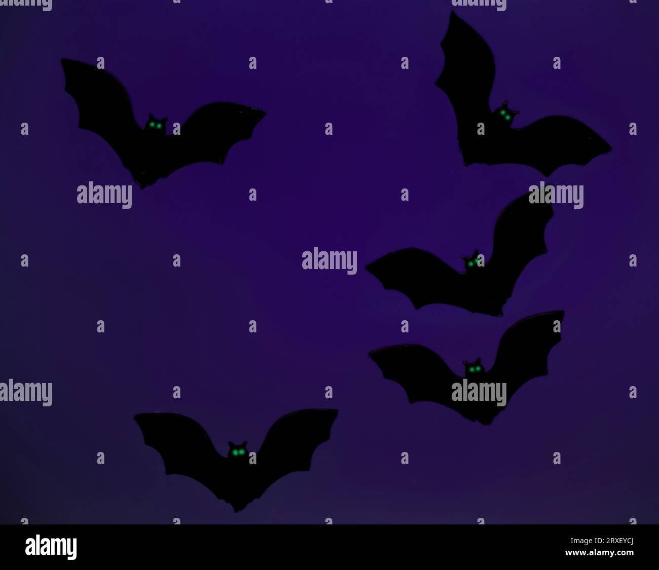 Chauves-souris en bois peintes en noir avec des yeux verts sur fond violet. Banque D'Images
