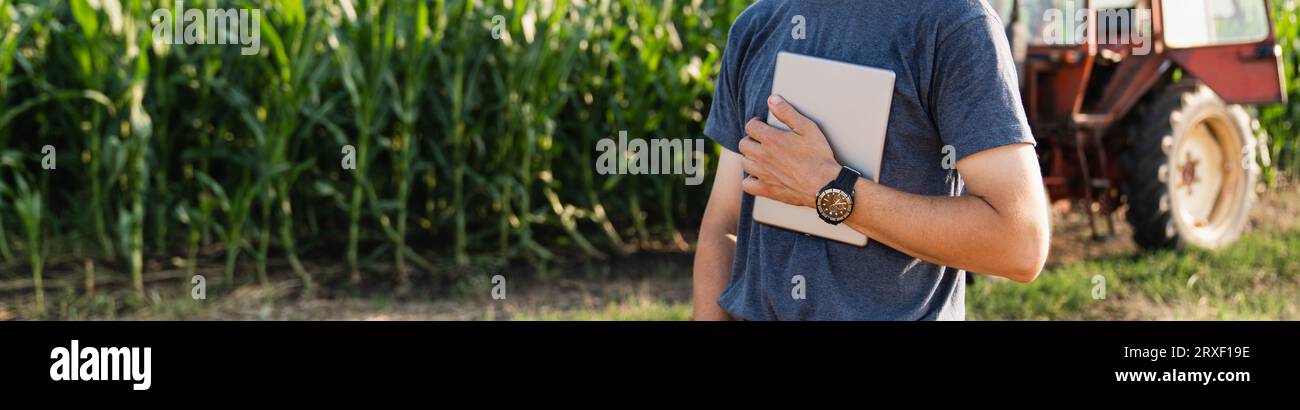 Agriculteur avec une tablette numérique est à côté d'un tracteur agricole.. Banque D'Images