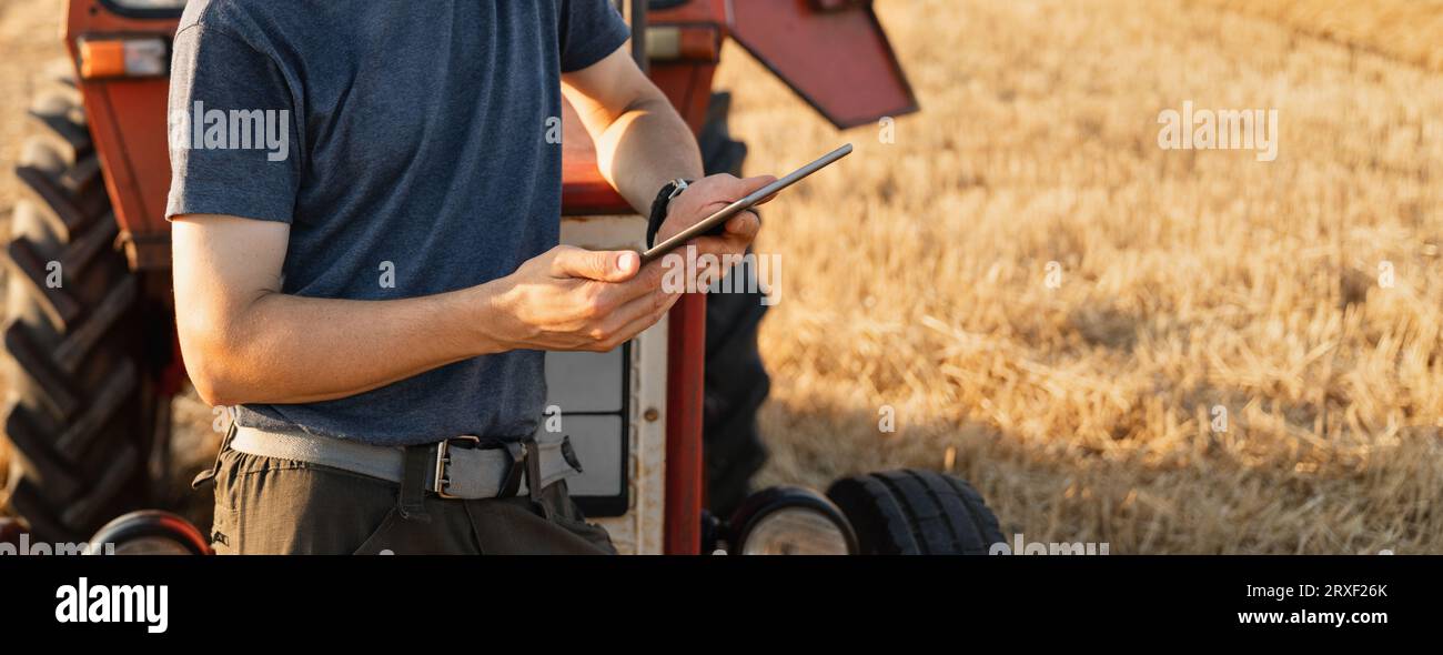 Agriculteur avec une tablette numérique est à côté d'un tracteur agricole.. Banque D'Images