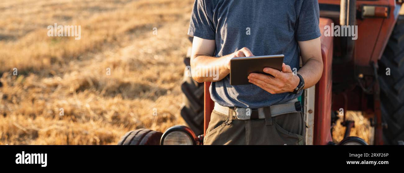 Agriculteur avec une tablette numérique est à côté d'un tracteur agricole.. Banque D'Images