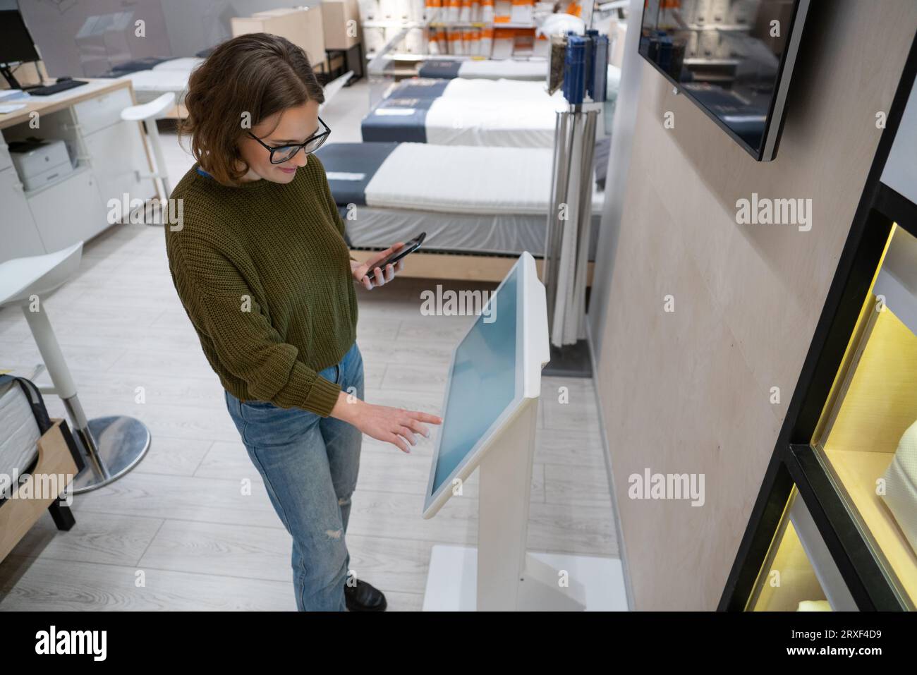 Femme avec le téléphone utilise le kiosque libre-service dans le centre commercial. Banque D'Images