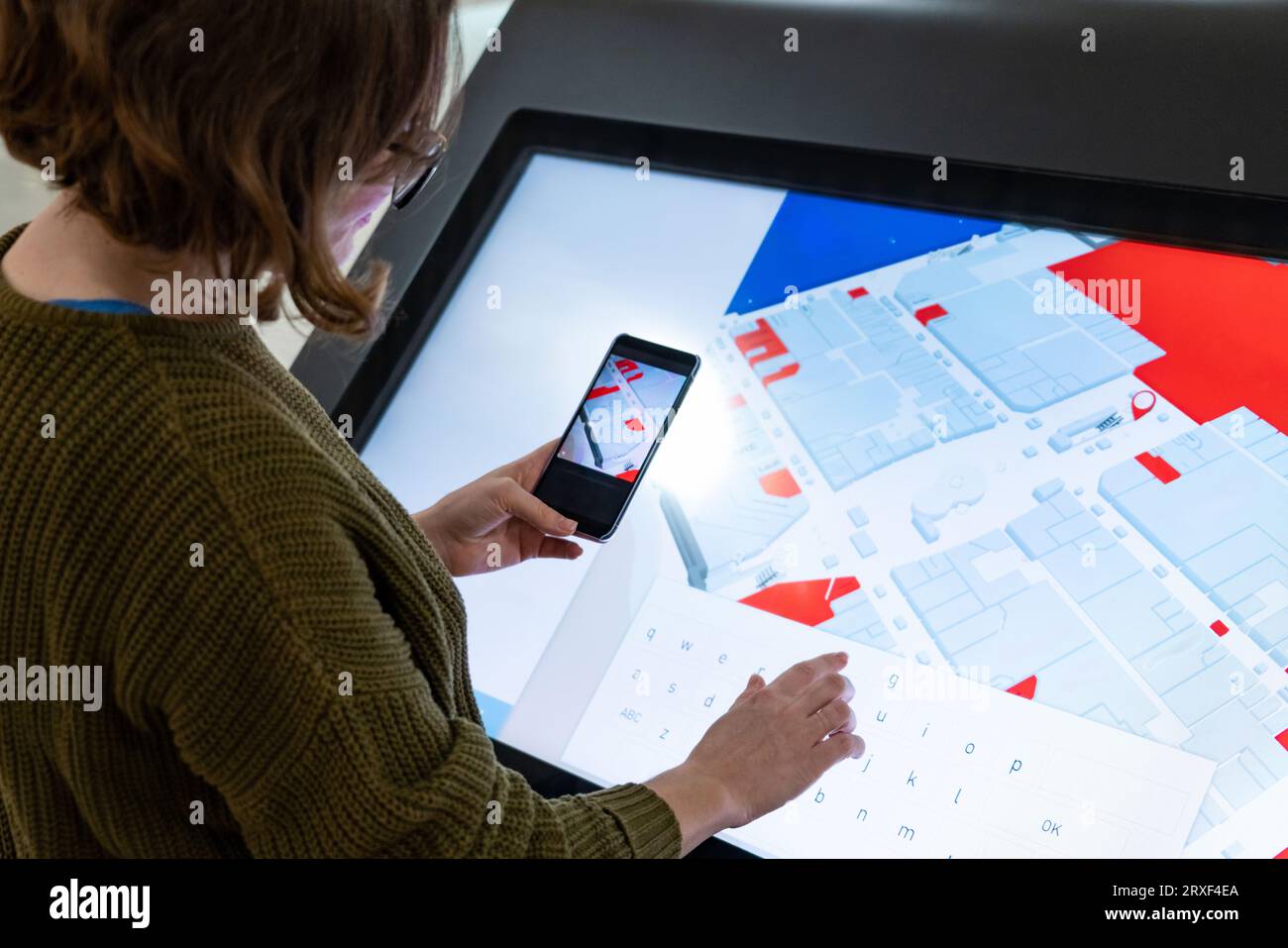 Femme avec le téléphone utilise le kiosque libre-service dans le centre commercial. Banque D'Images