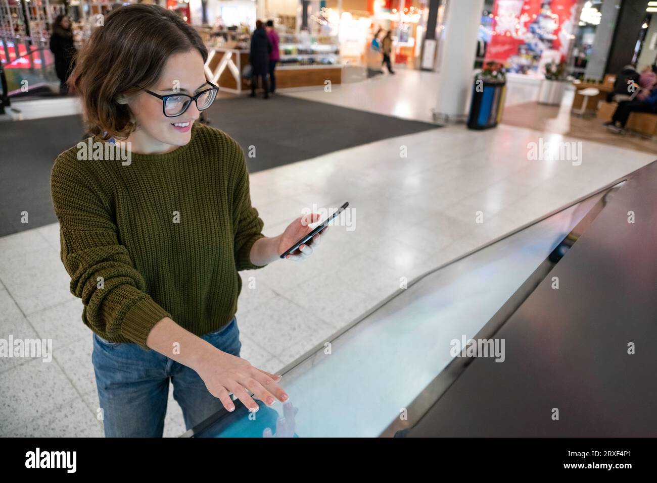 Femme avec le téléphone utilise le kiosque libre-service dans le centre commercial. Banque D'Images