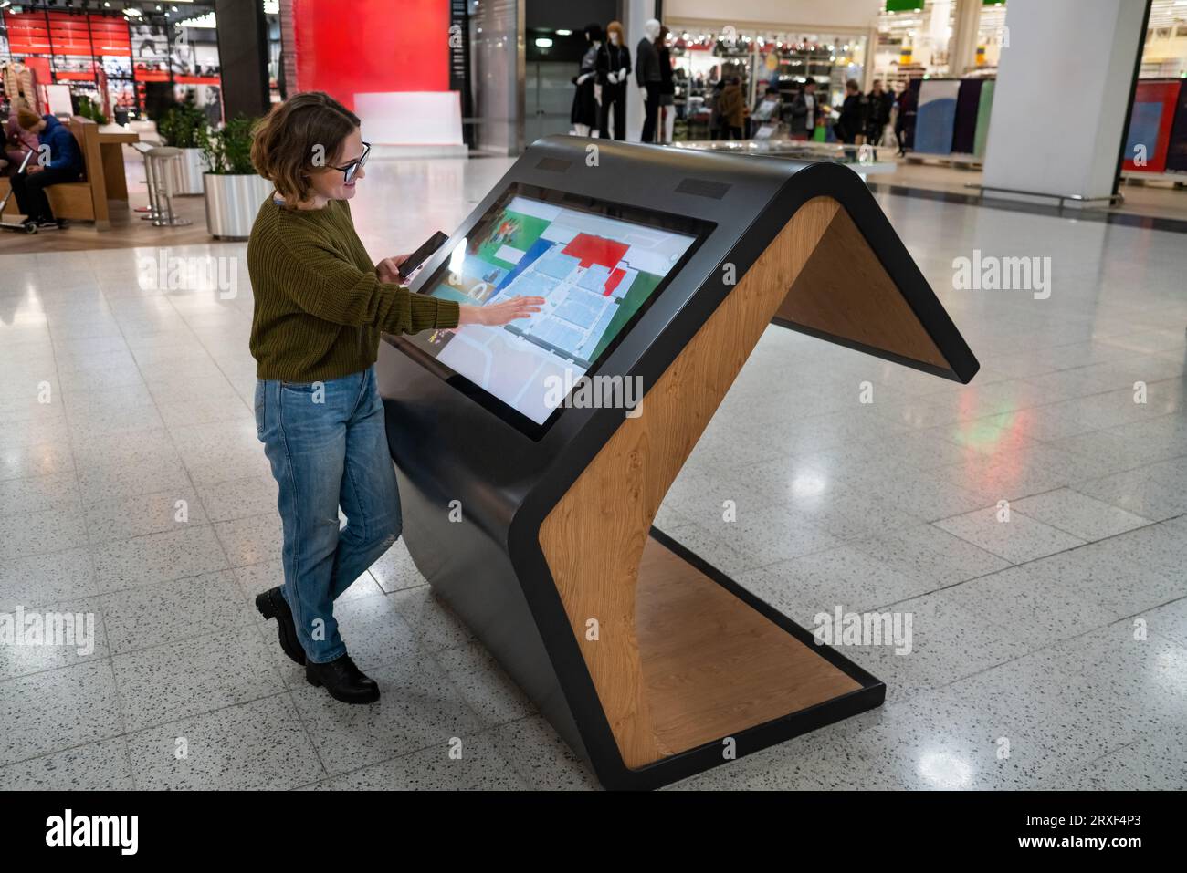 Femme avec le téléphone utilise le kiosque libre-service dans le centre commercial. Banque D'Images
