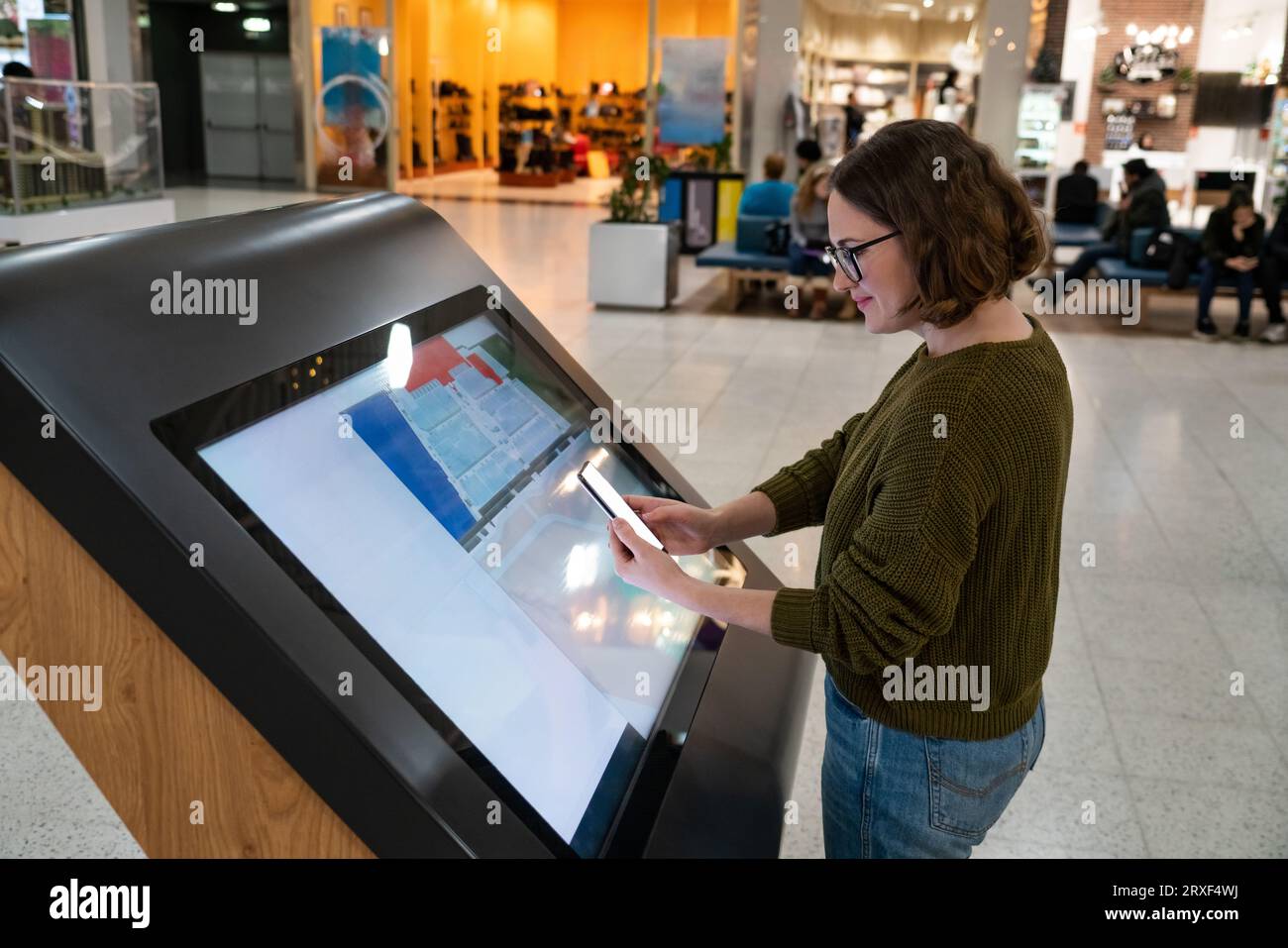 Femme avec le téléphone utilise le kiosque libre-service dans le centre commercial. Banque D'Images