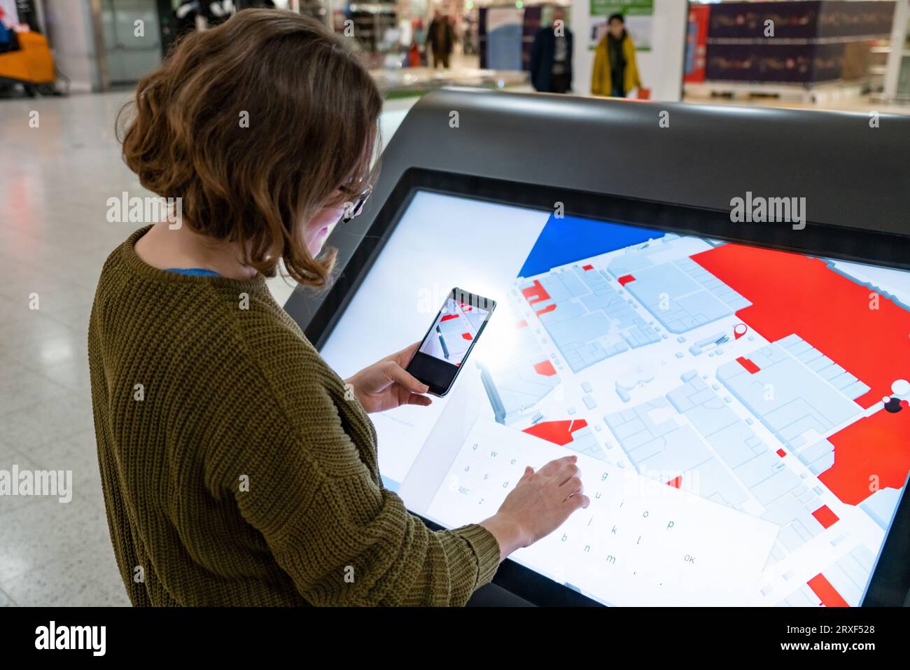 Femme avec le téléphone utilise le kiosque libre-service dans le centre commercial. Banque D'Images