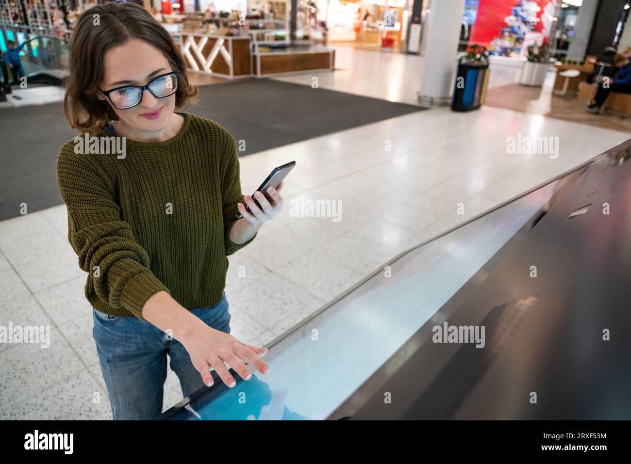 Femme avec le téléphone utilise le kiosque libre-service dans le centre commercial. Banque D'Images