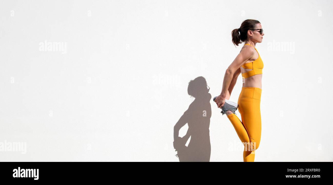 Femme sportive faisant des exercices d'échauffement, étirement des jambes contre un fond de mur blanc Banque D'Images