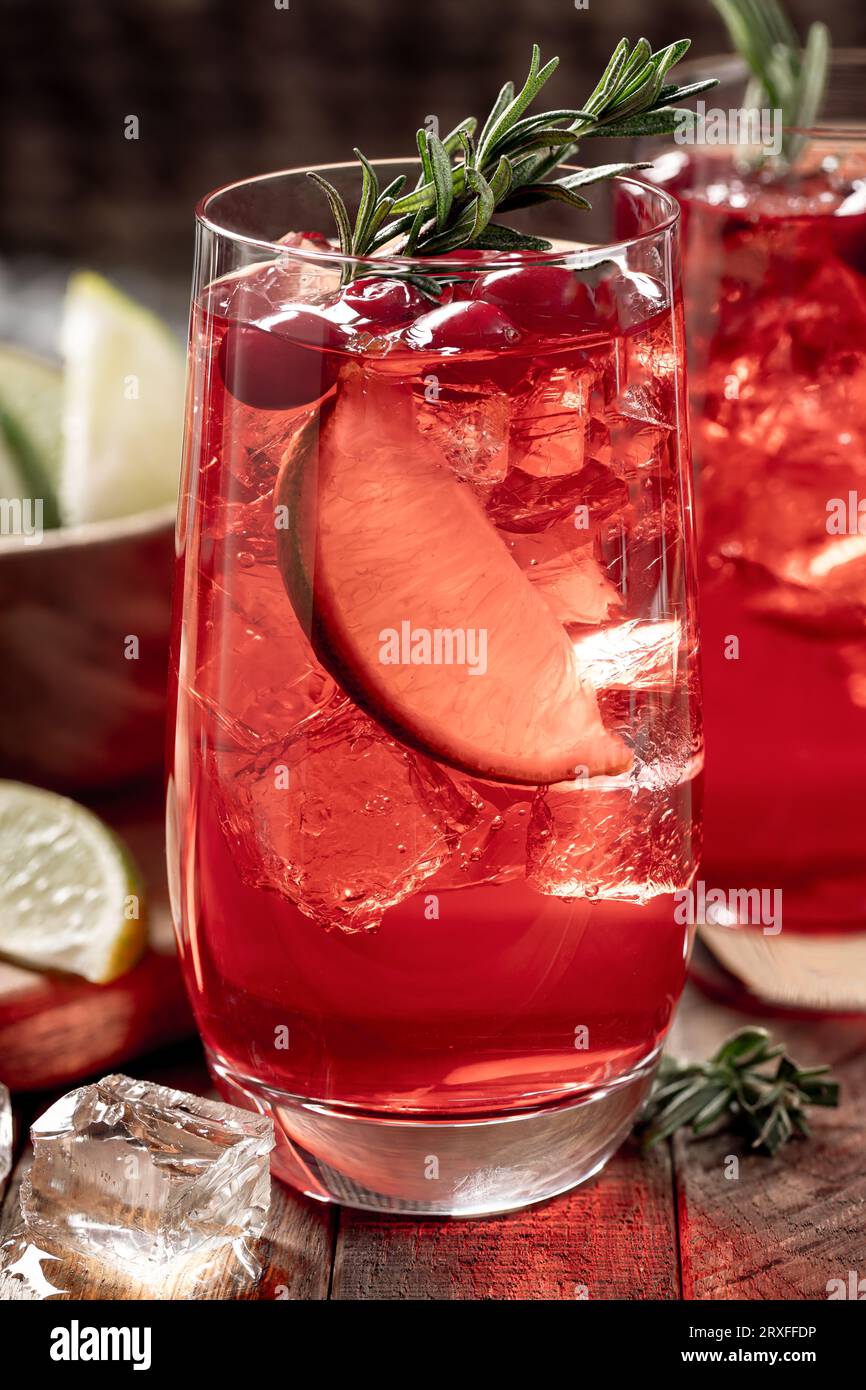 Cocktail de canneberges avec des tranches de citron vert et garni de romarin sur une table en bois rustique Banque D'Images