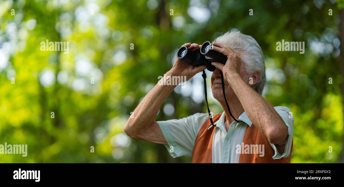 Homme âgé passant du temps libre à l'extérieur dans la nature, observant les animaux de la forêt avec des jumelles. Banque D'Images