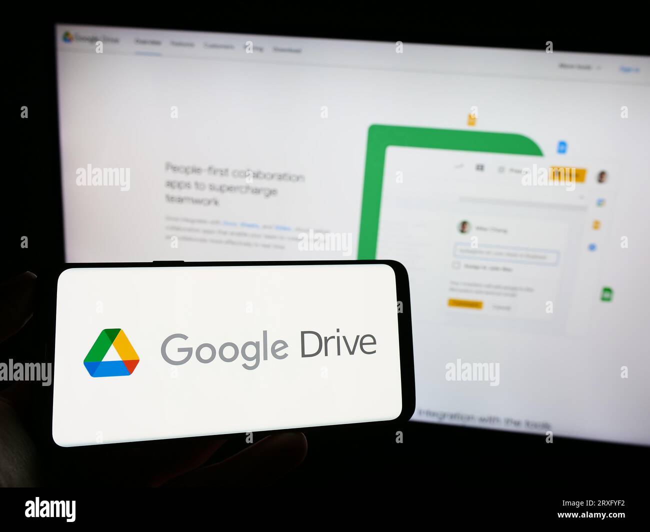 Personne tenant le téléphone mobile avec le logo de la plate-forme de stockage de fichiers Google Drive sur l'écran en face de la page Web de l'entreprise. Concentrez-vous sur l'affichage du téléphone. Banque D'Images