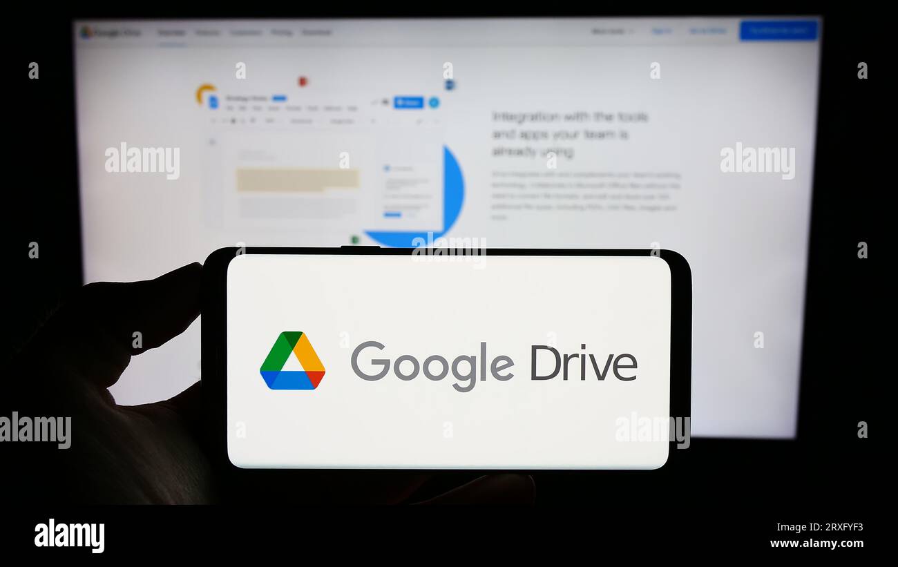 Personne tenant le téléphone portable avec le logo de la plate-forme de stockage de fichiers Google Drive sur l'écran en face de la page Web de l'entreprise. Concentrez-vous sur l'affichage du téléphone. Banque D'Images