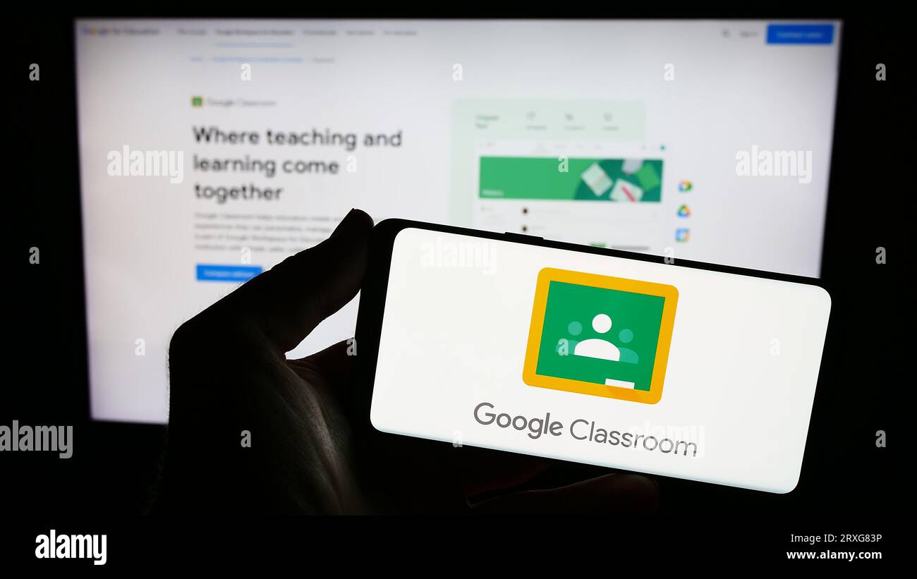 Personne tenant le smartphone avec le logo de la plate-forme d'apprentissage mixte Google Classroom sur l'écran en face du site Web. Concentrez-vous sur l'affichage du téléphone. Banque D'Images