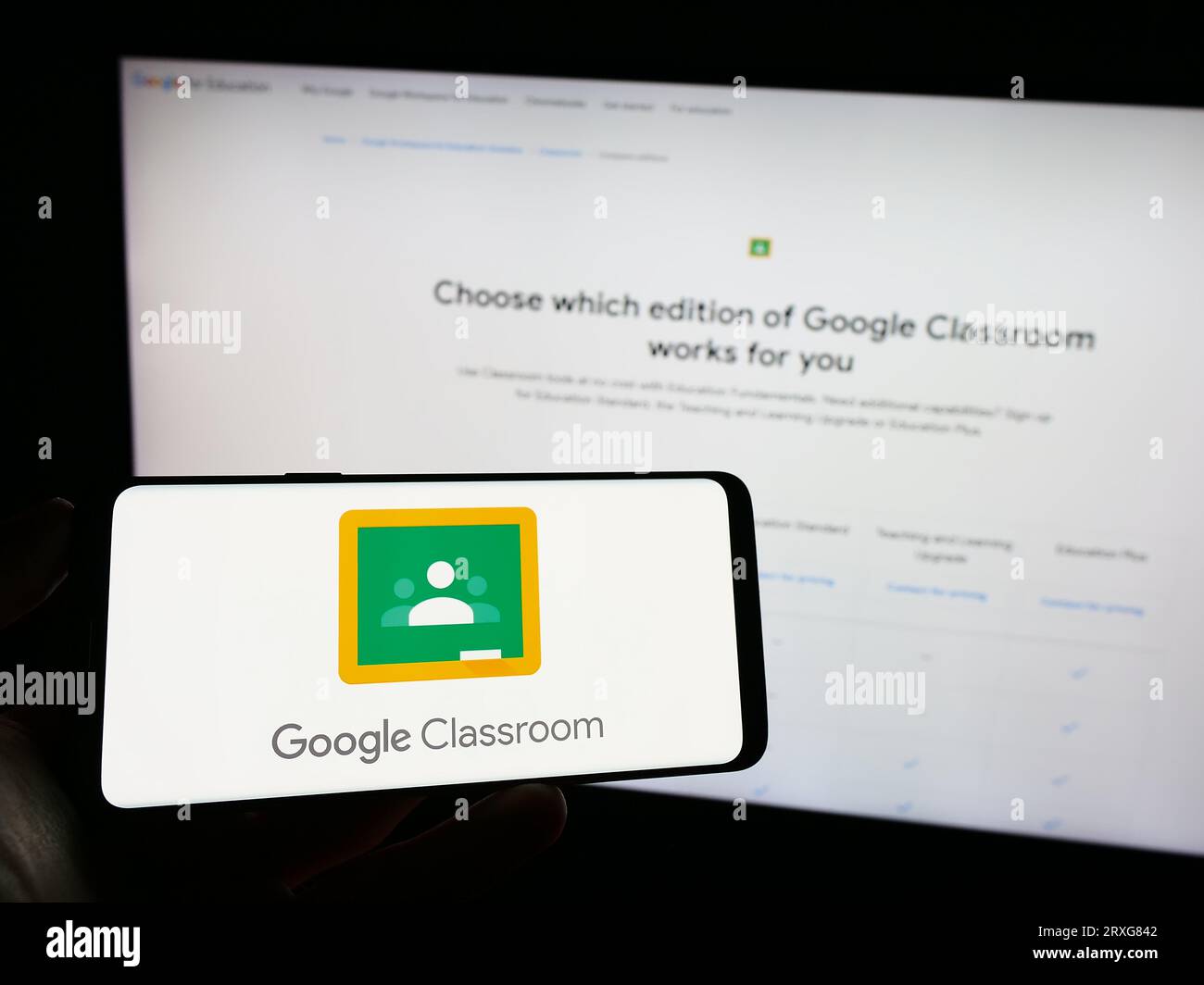 Personne tenant le téléphone mobile avec le logo de la plate-forme d'apprentissage mixte Google Classroom sur l'écran en face de la page Web. Concentrez-vous sur l'affichage du téléphone. Banque D'Images