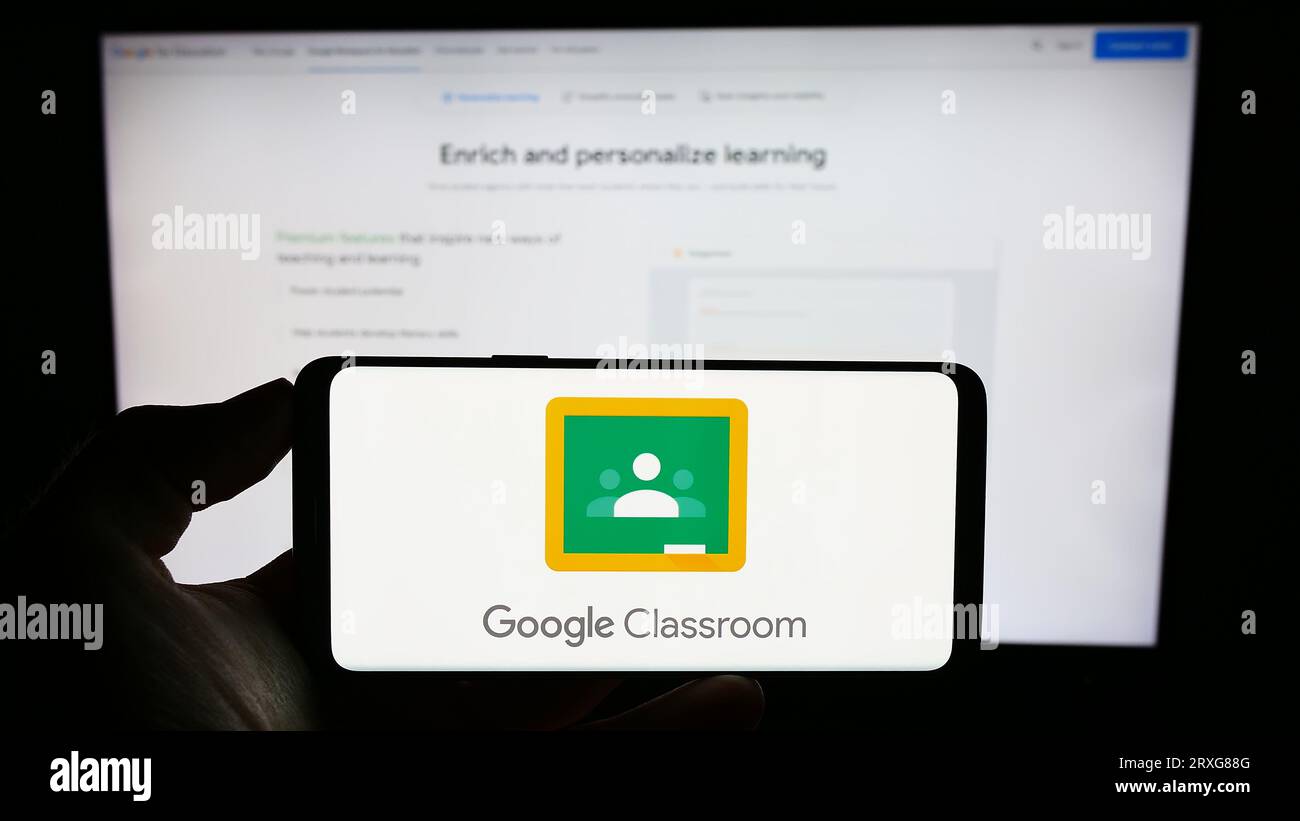 Personne tenant le téléphone portable avec le logo de la plate-forme d'apprentissage mixte Google Classroom sur l'écran en face de la page Web de l'entreprise. Concentrez-vous sur l'affichage du téléphone. Banque D'Images