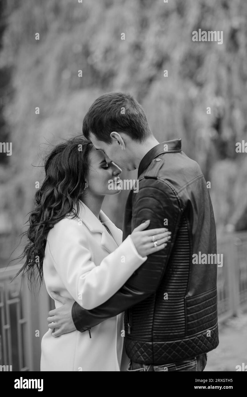 Un homme embrasse sa femme enceinte. Un homme dans une veste noire embrasse et embrasse une femme dans un manteau blanc. Automne Banque D'Images
